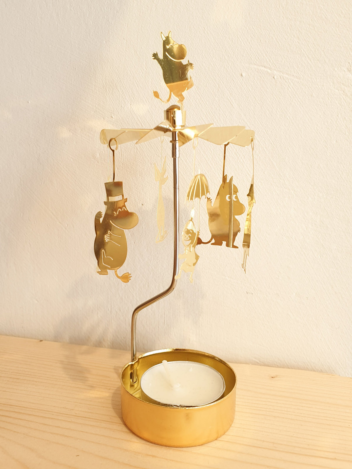 Gold Moomin Änglaspel on a wooden surface against a cream wall
