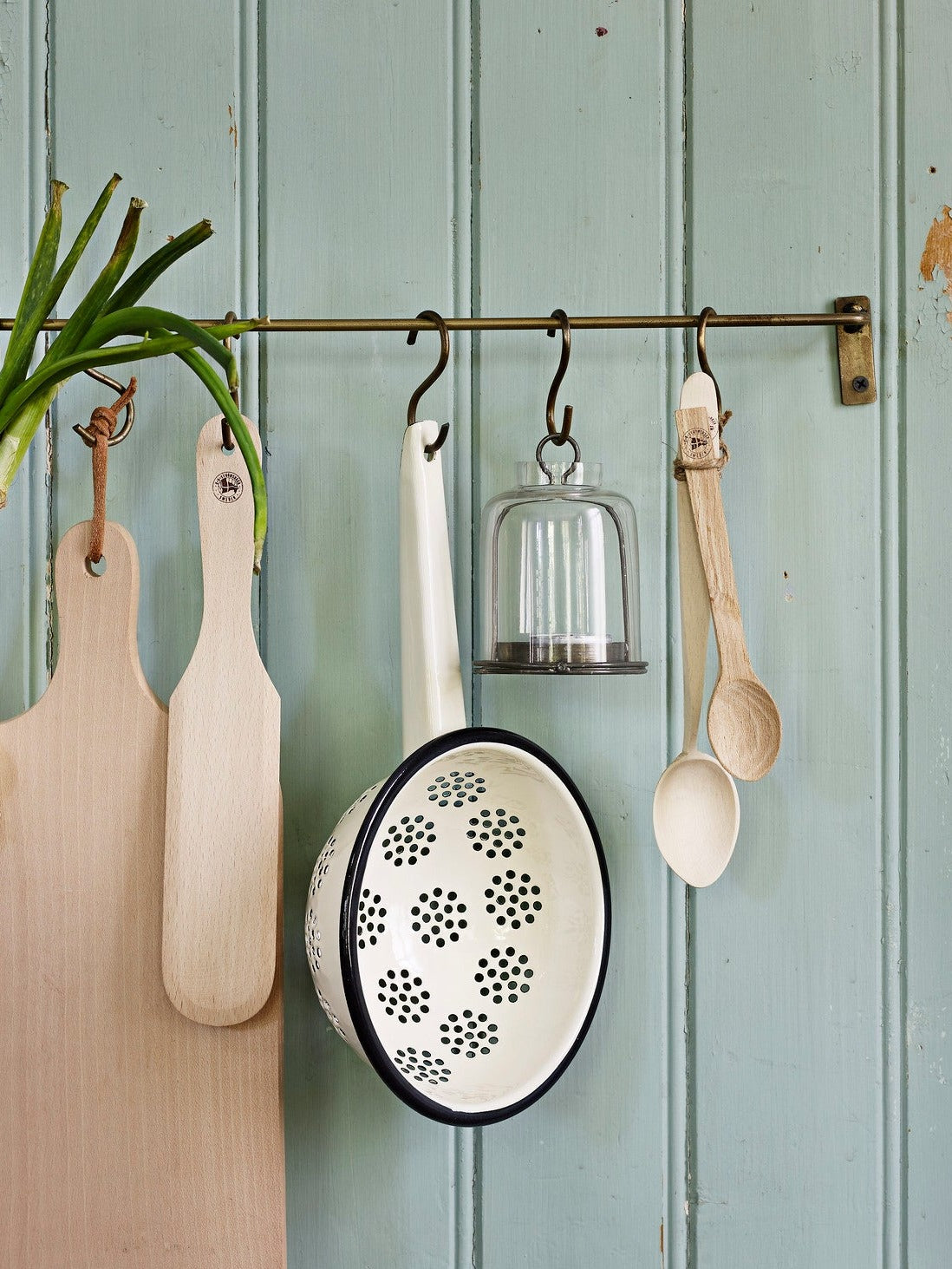 Strömshaga Emil's enamel colander hung on kitchen rail with wooden boards and utensils against sage green wall