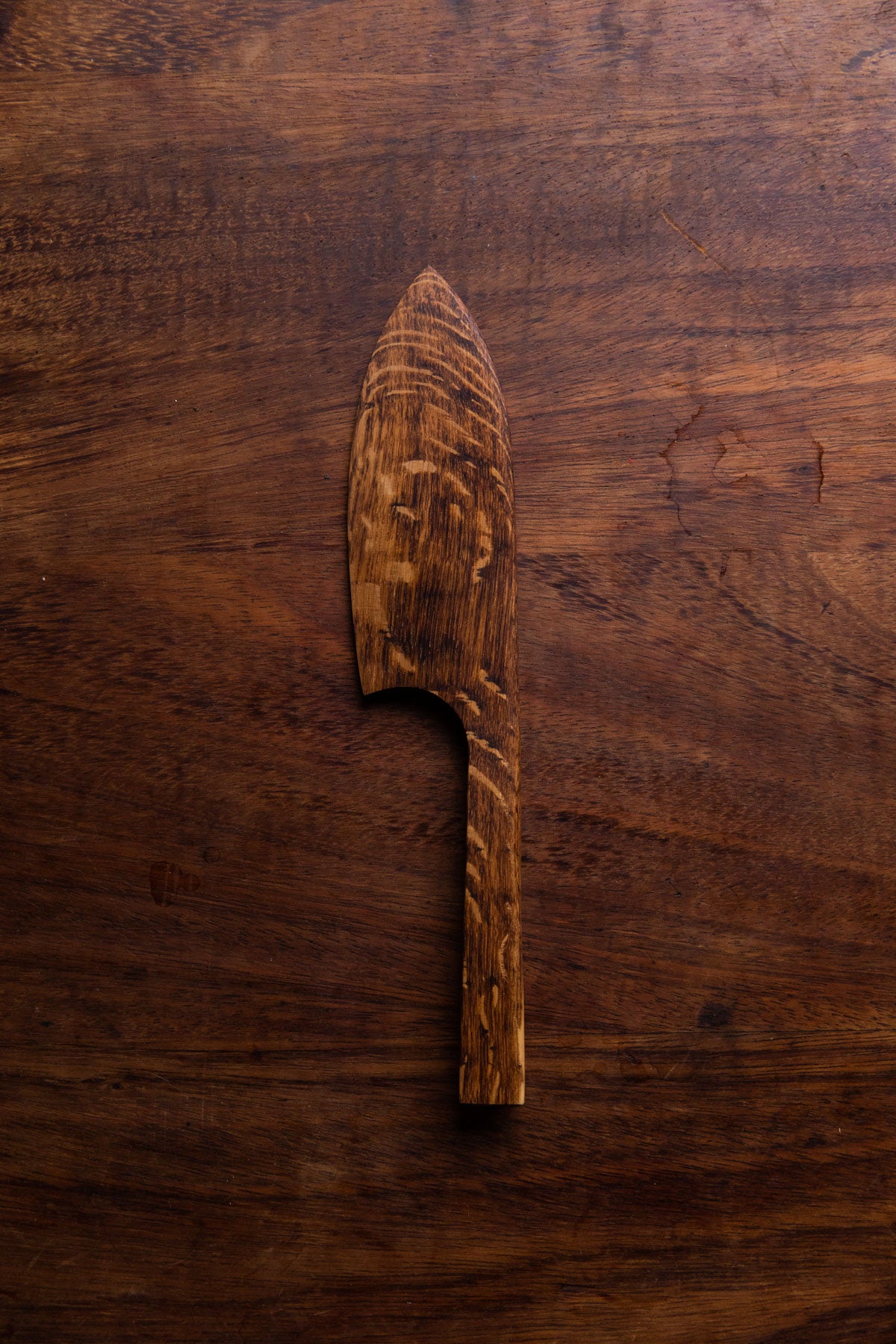 A brown English Oak cake knife sits against a dark brown wooden tabletop.