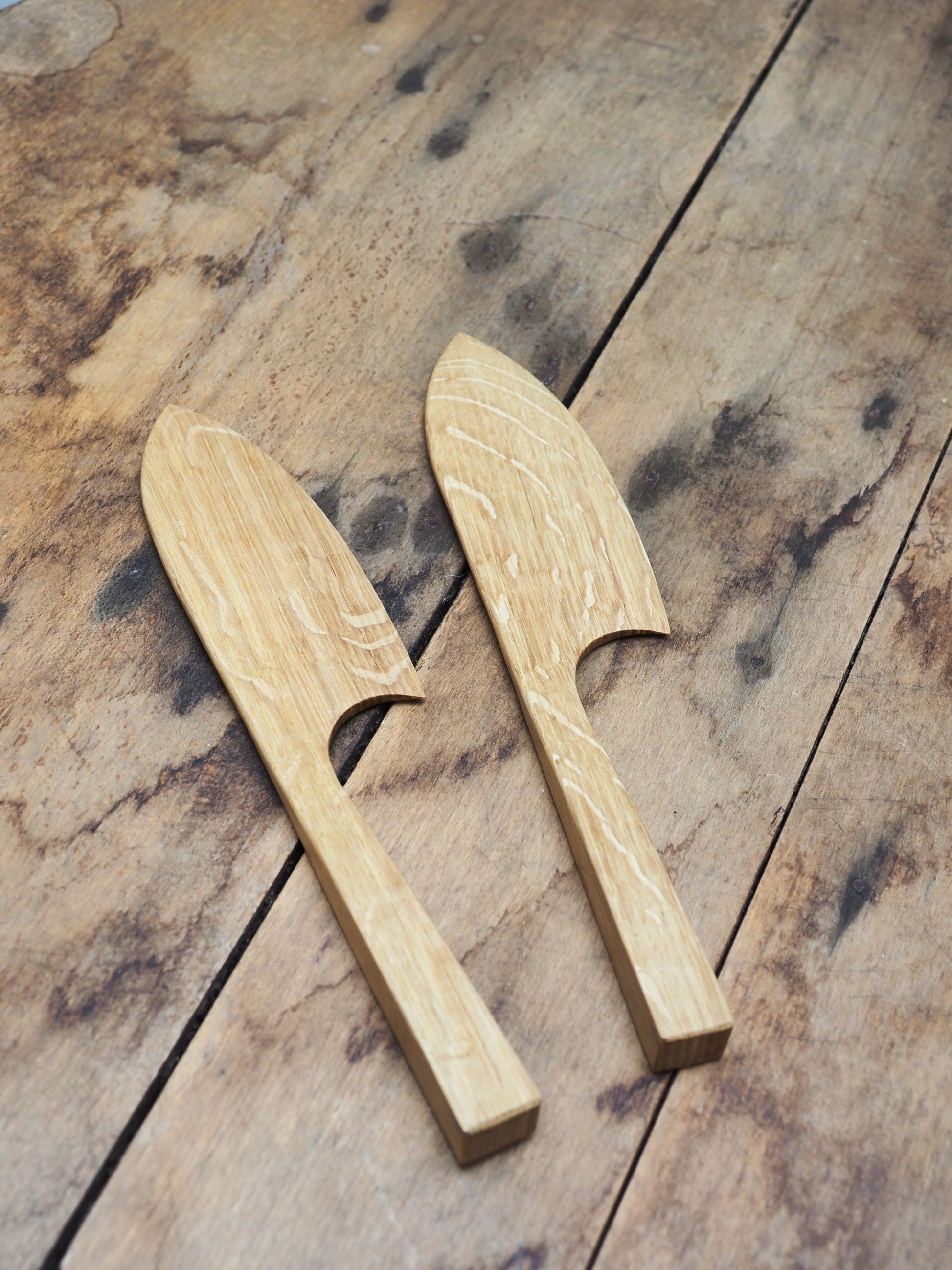 Two English Oak cake knifes laid down on a wooden table.