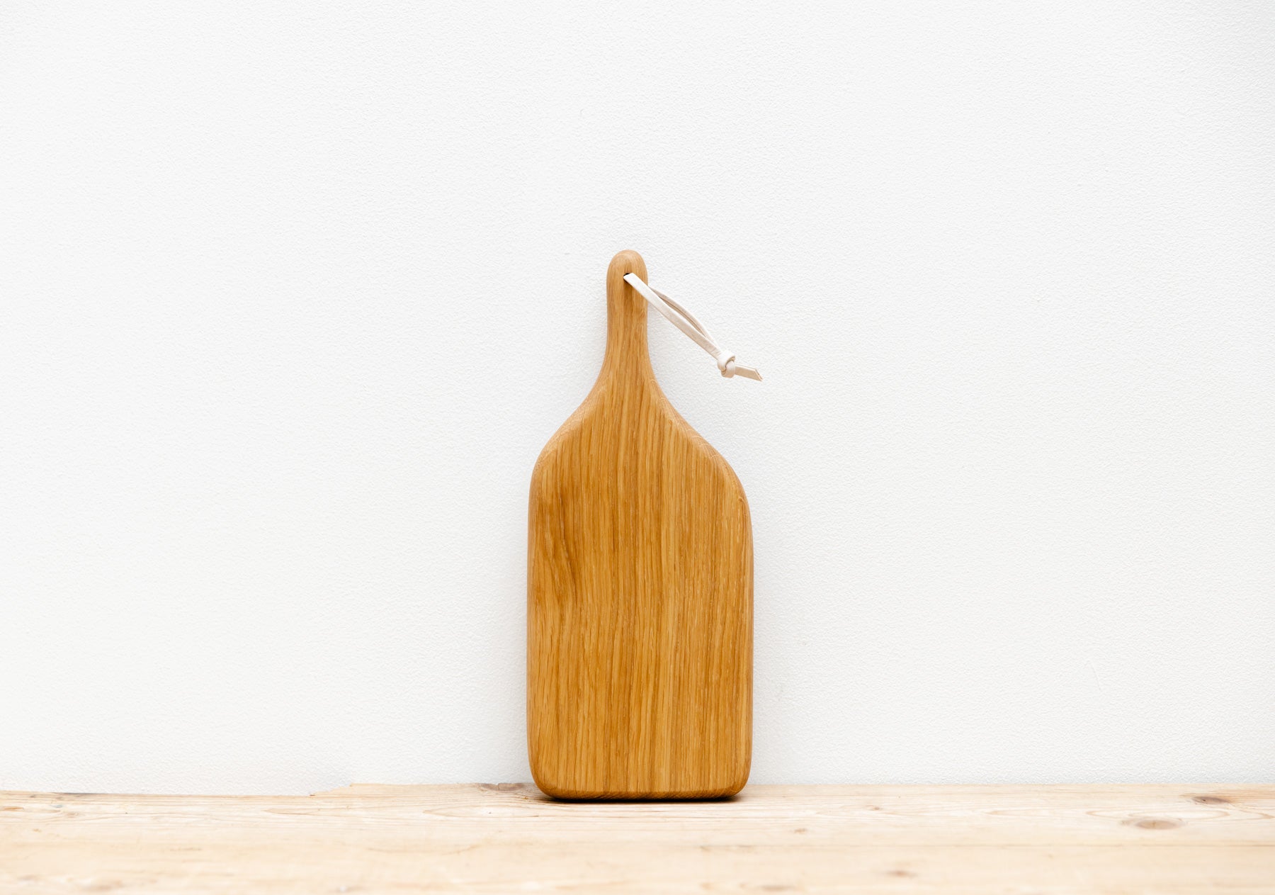 An English Oak mini board is resting up against a white background, sitting on a light wooden table top.