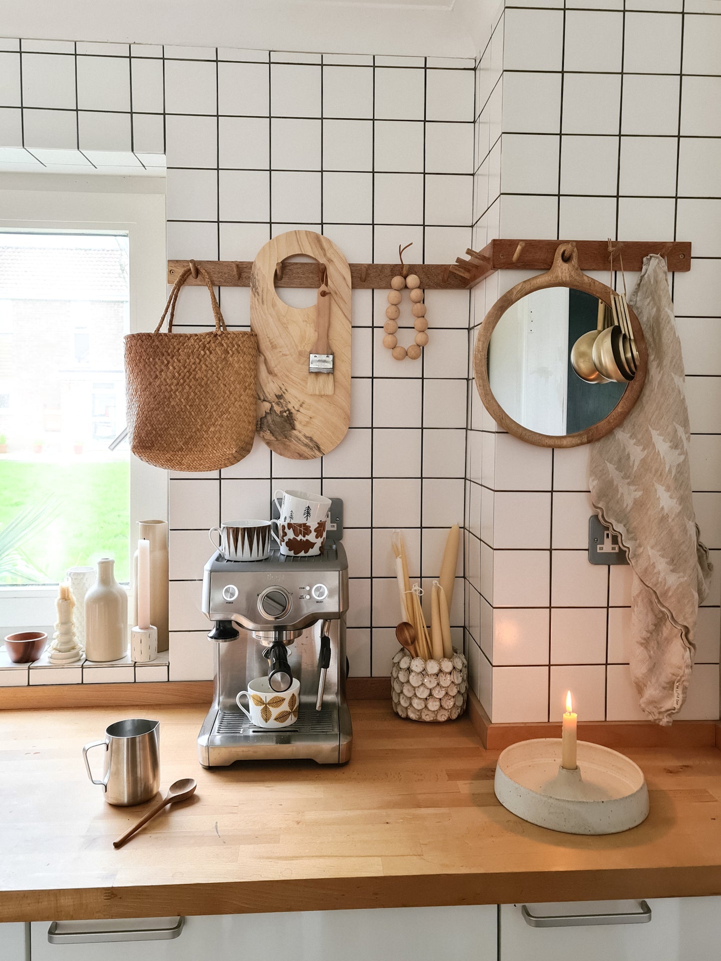 A white tiled, modern kitchen, with a wooden peg rail and hanging objects.