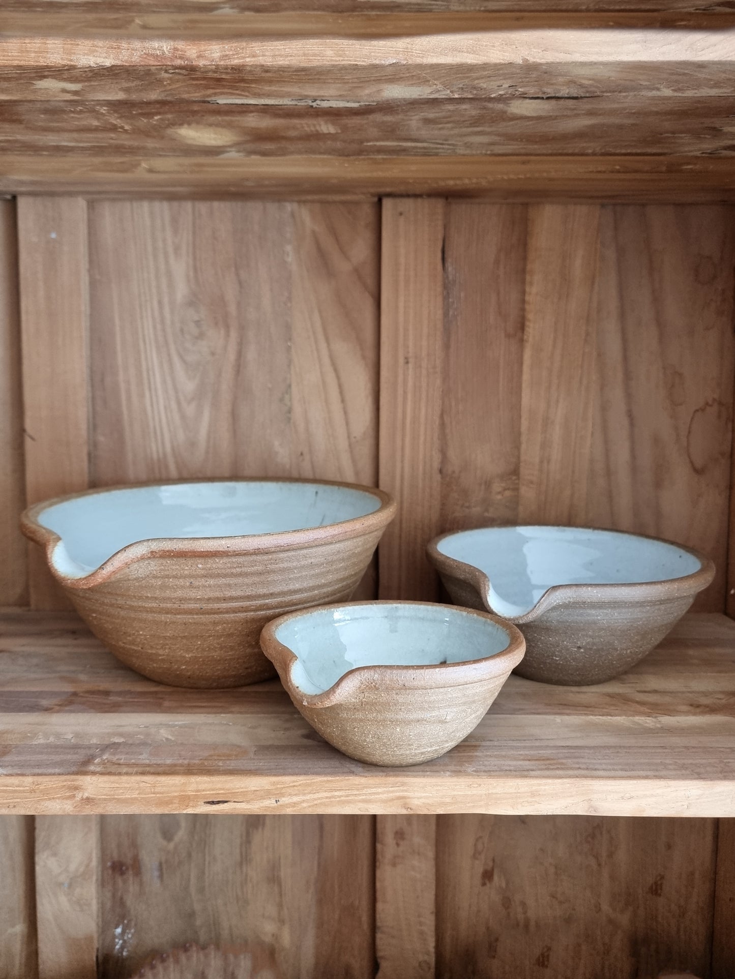 A set of three Leach Pottery mixing bowls in three different sizes displayed on a wooden shelf.