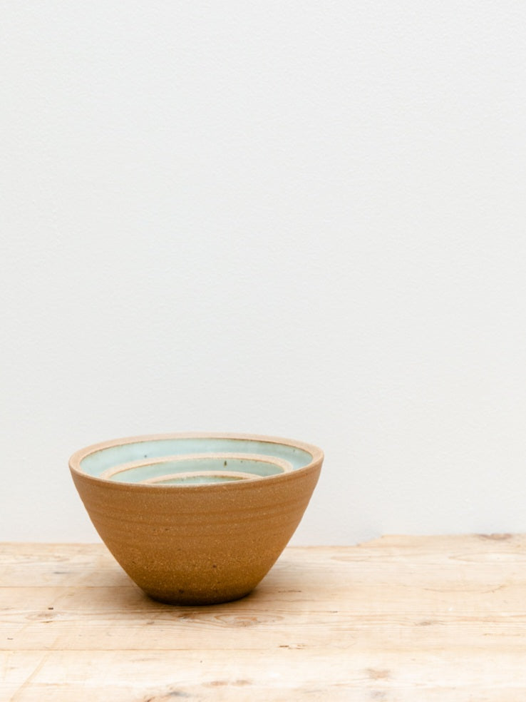 Three Leach Pottery prepping bowls nesting inside of one another on a wooden table with a white background.
