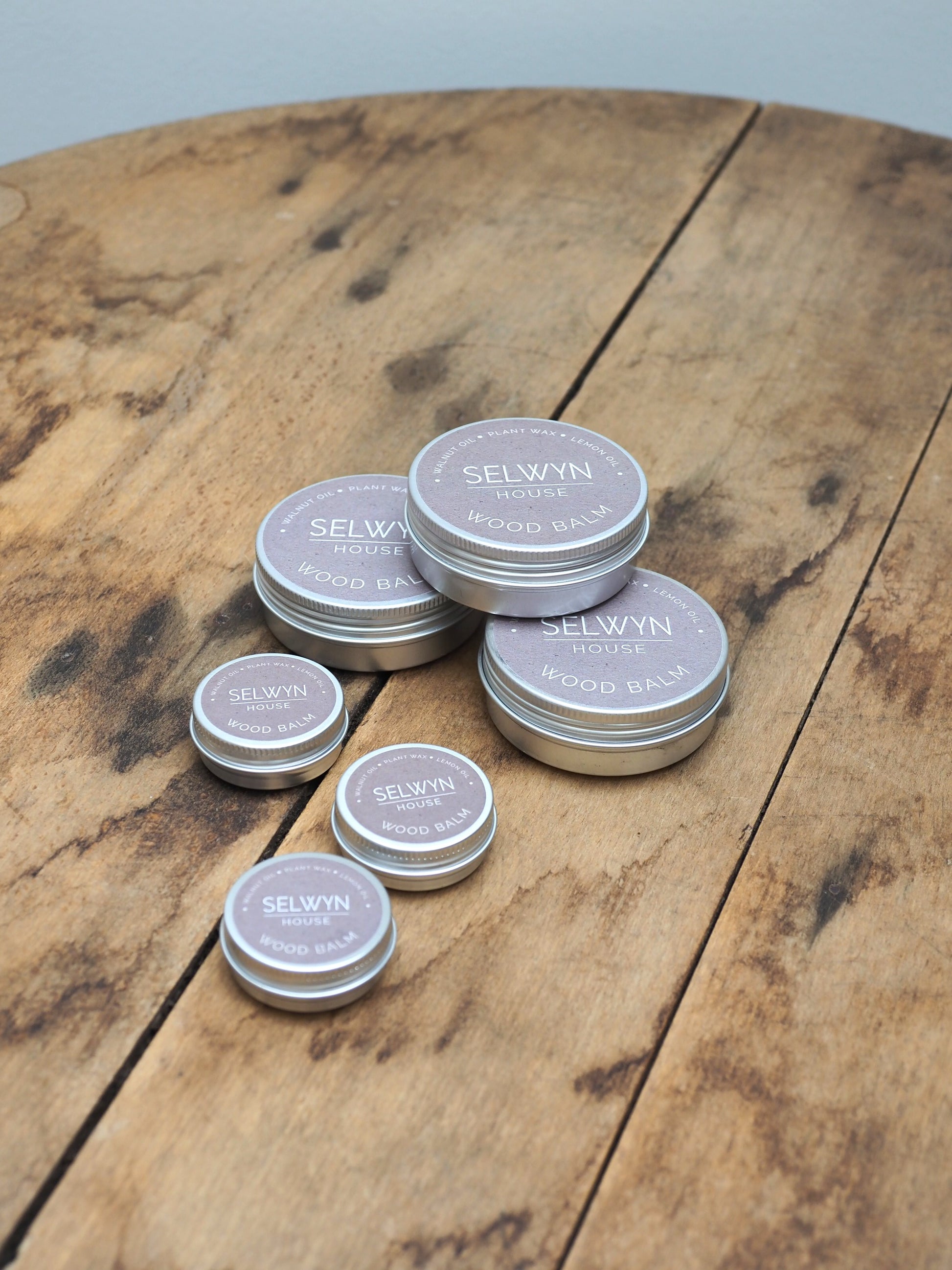 Three tins of small wood balm and three tins of large wood balm are placed on a wooden table.