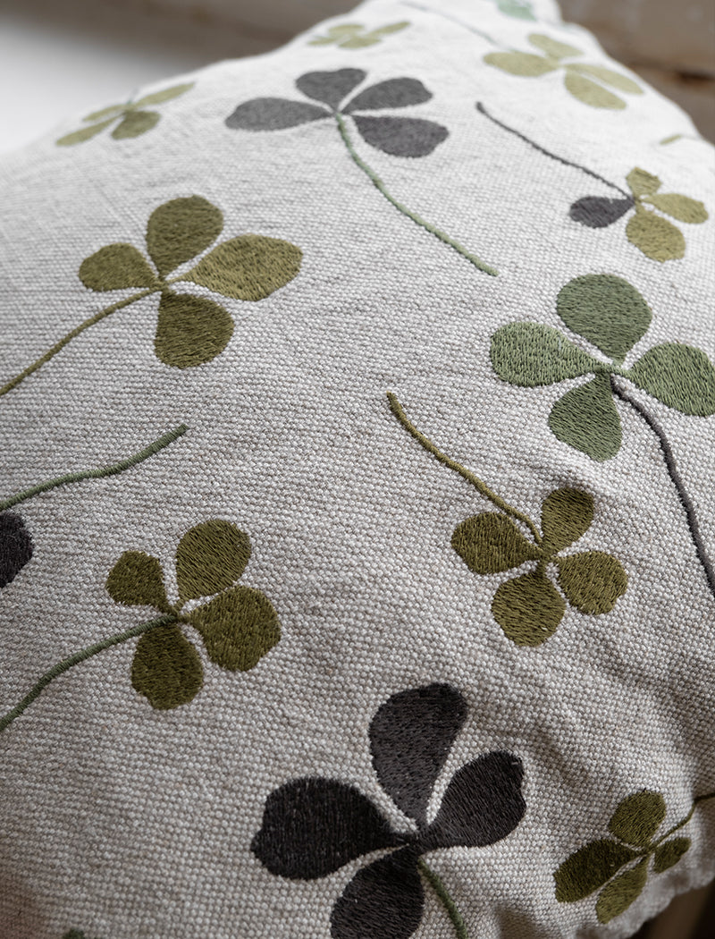 Close up of a linen coloured cushion with a green clover embroidery pattern.