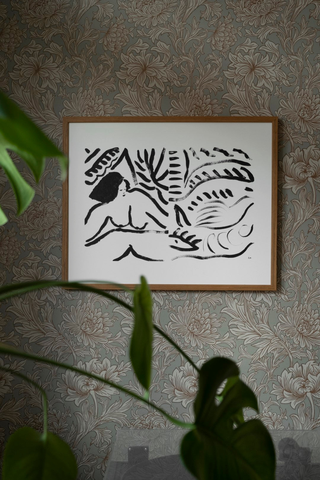 A framed poster featuring a black and white abstract artwork, hanging on a patterned wallpaper wall.