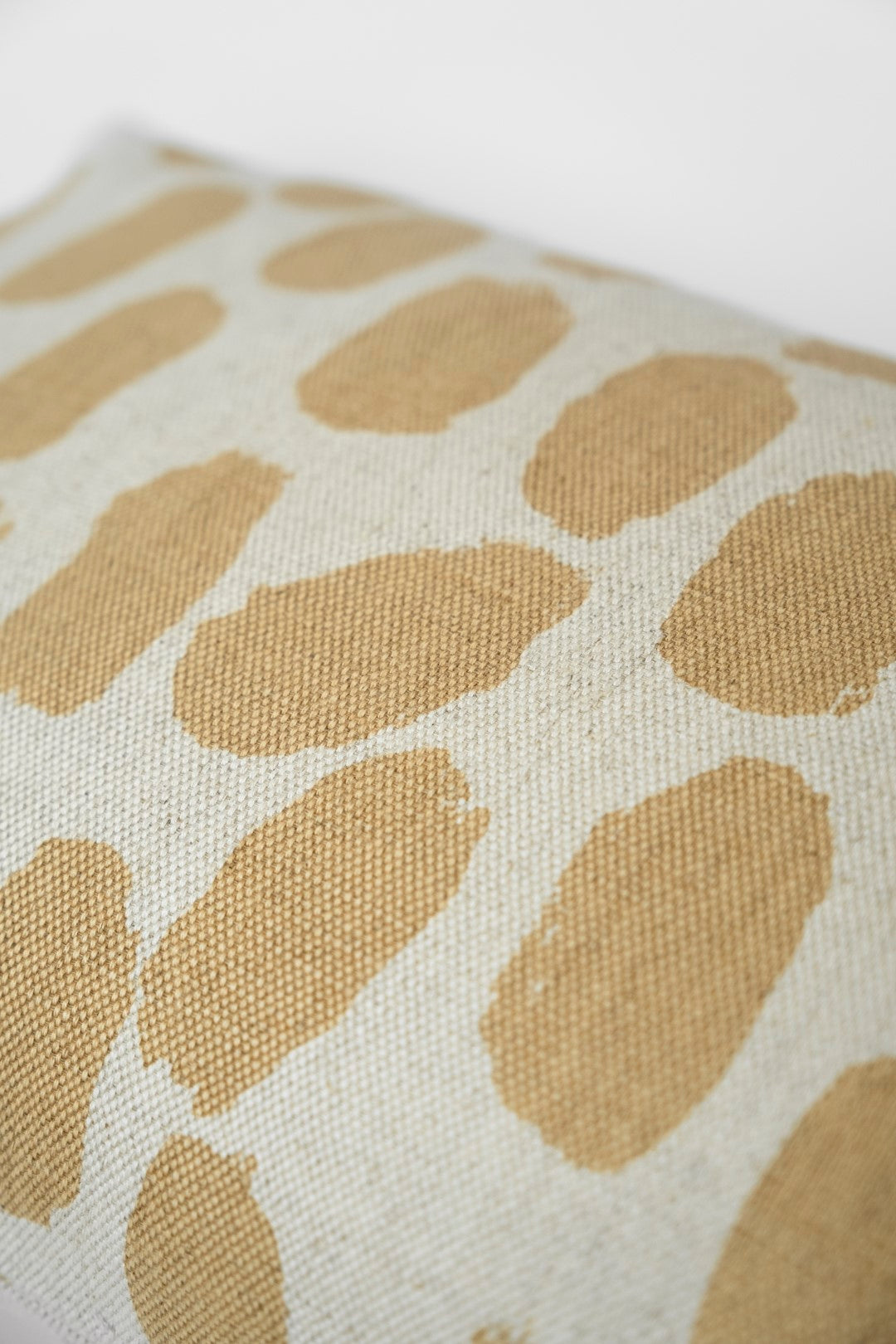 Close up of a cushion with a dotted pattern in a white and sand colourway against a white background.