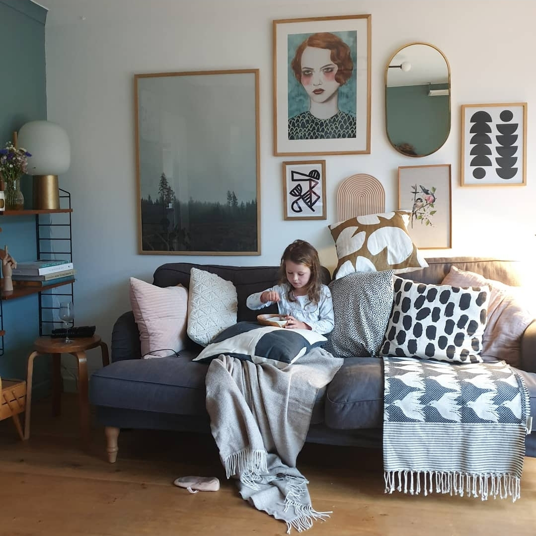 Young child sat on a sofa, surrounded by blankets and cushions and framed images on the wall behind.