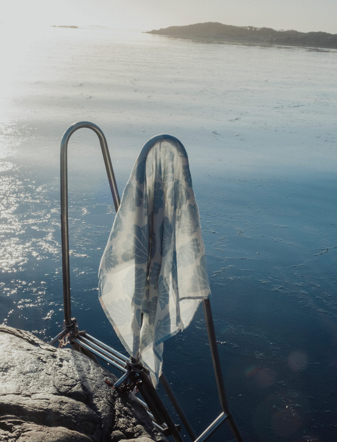 Aqua snacka blanket from Fine Little Day hanging off a metal ladder going into the sea.