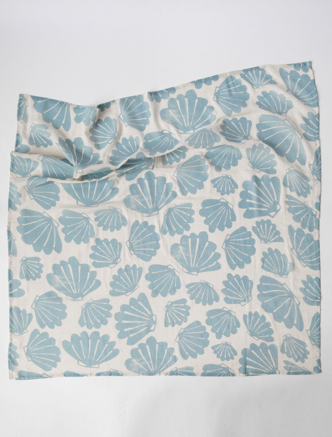 Aqua snacka muslin blanket featuring a shell pattern outstretched onto a white background.