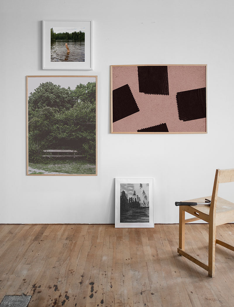Framed prints on white wall, with another print resting on the floor and a wooden chair.