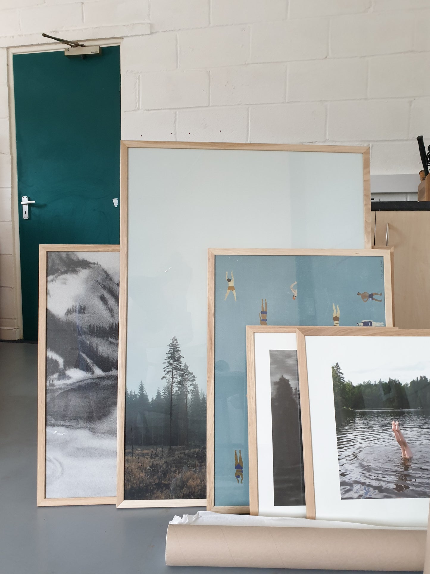 Gathering of framed prints and posters in a warehouse with a green door in the background.