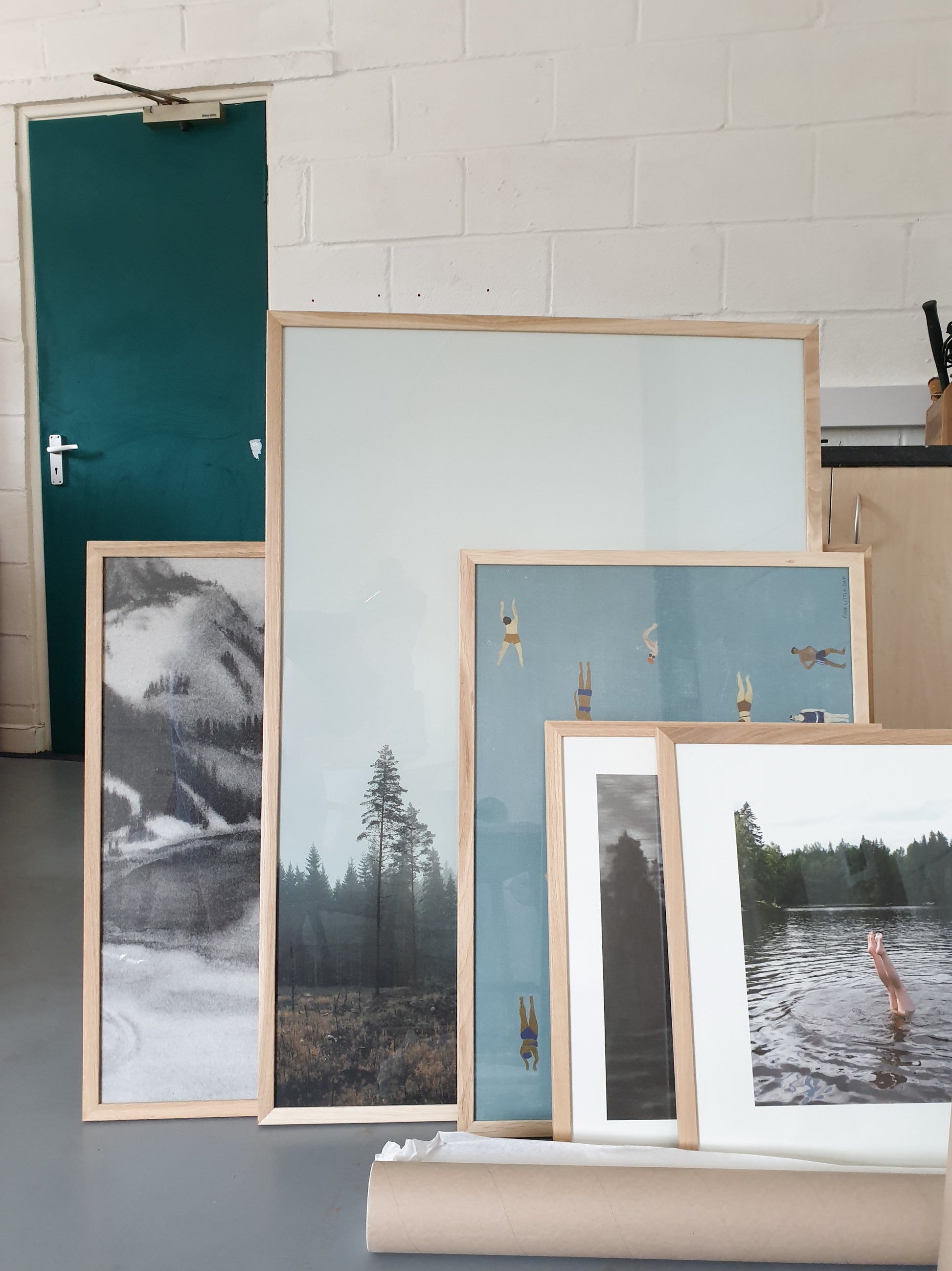 Gathering of framed prints and posters in a warehouse with a green door in the background.
