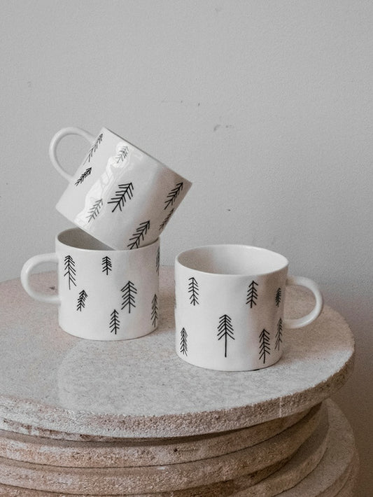 Three white porcelain cups with pine tree motifs placed on a stack of marble boards.
