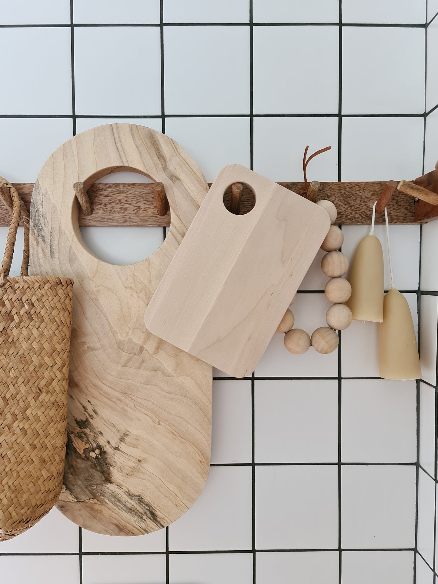 Birch sandwich platter hanging on a peg rail with various other kitchen items surrounding it against a tiled background.