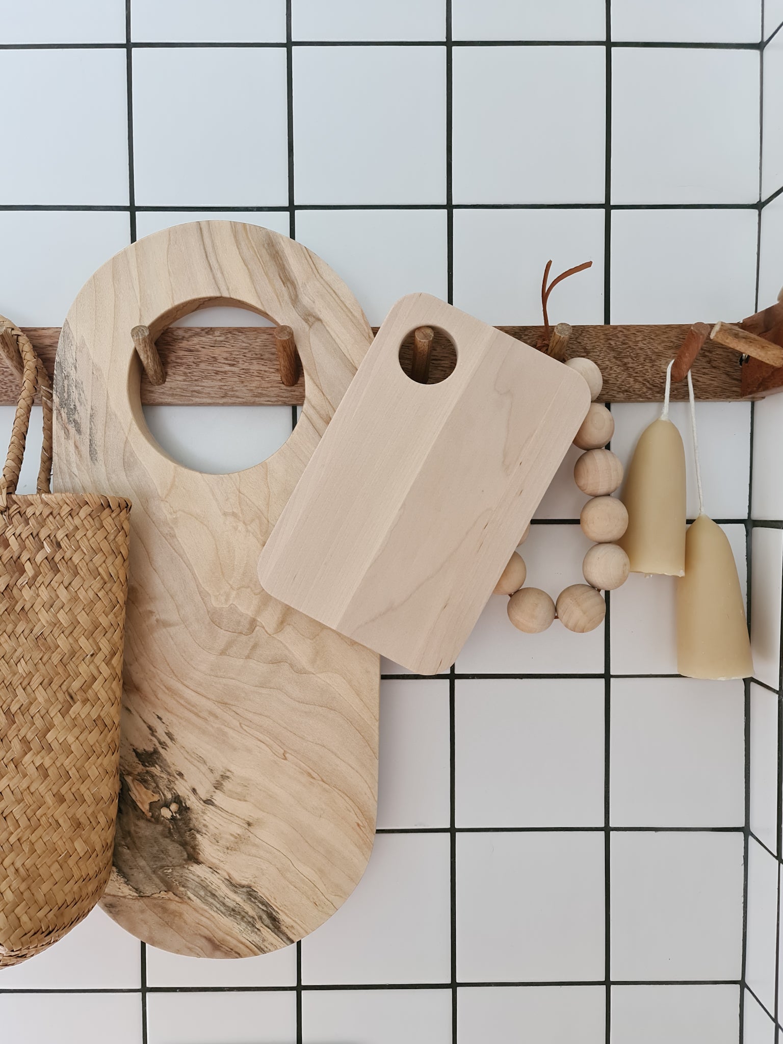 Birch sandwich platter hanging on a peg rail with various other kitchen items surrounding it against a tiled background.