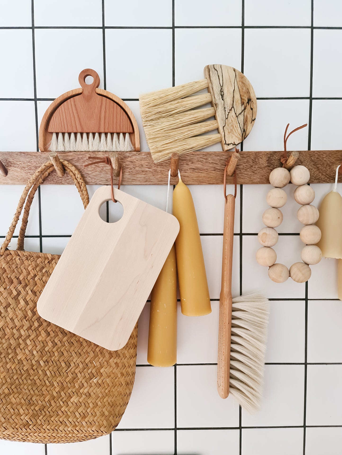 Birch sandwich platter hanging on a peg rail with various other kitchen items surrounding it against a tiled background.