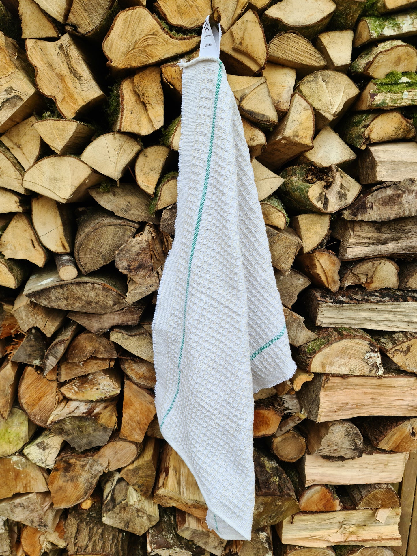 A white cleaning cloth with green stripes hanging against chopped wood.