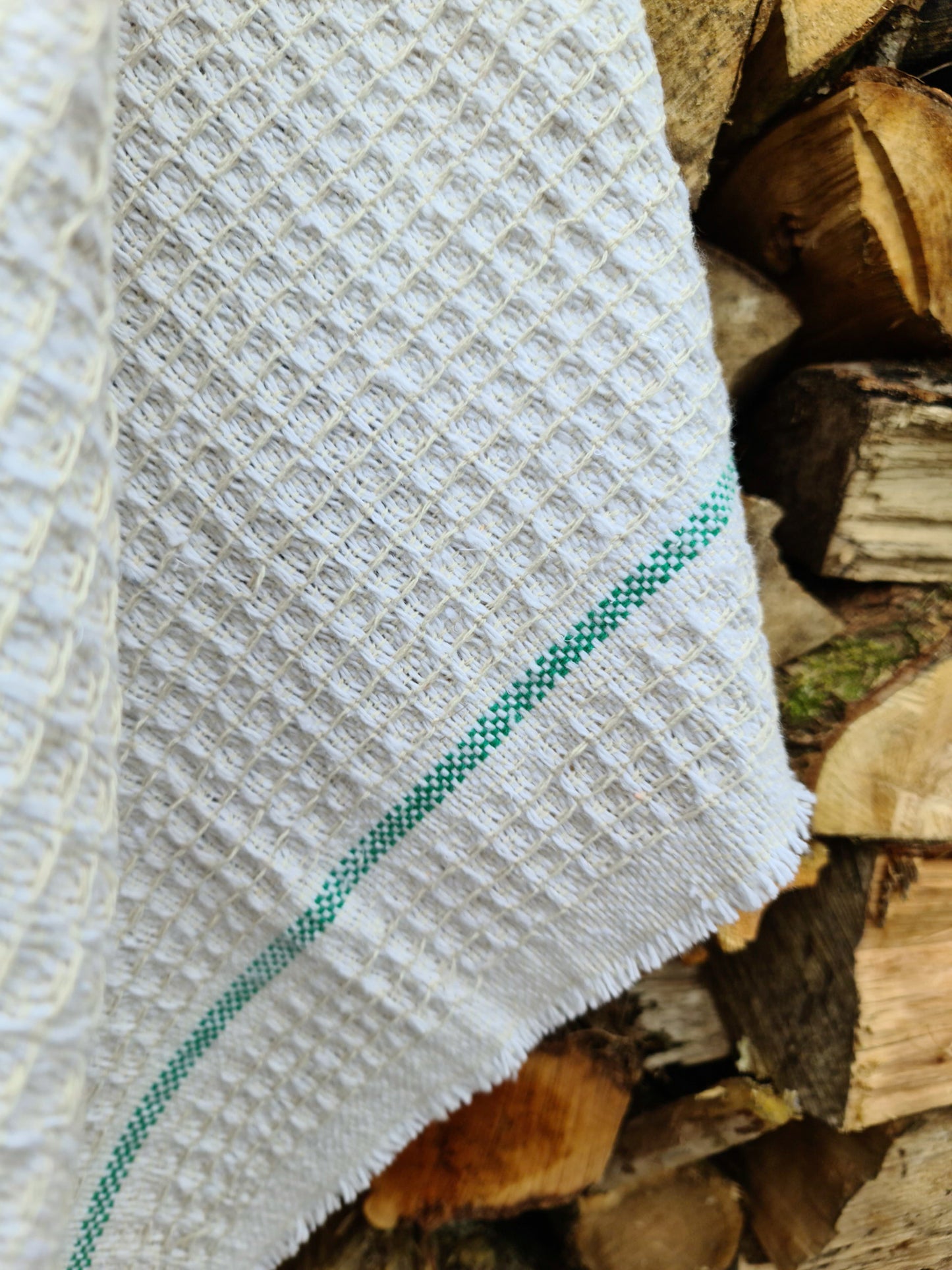 Close up of a white cleaning cloth with green stripes hanging against chopped wood.