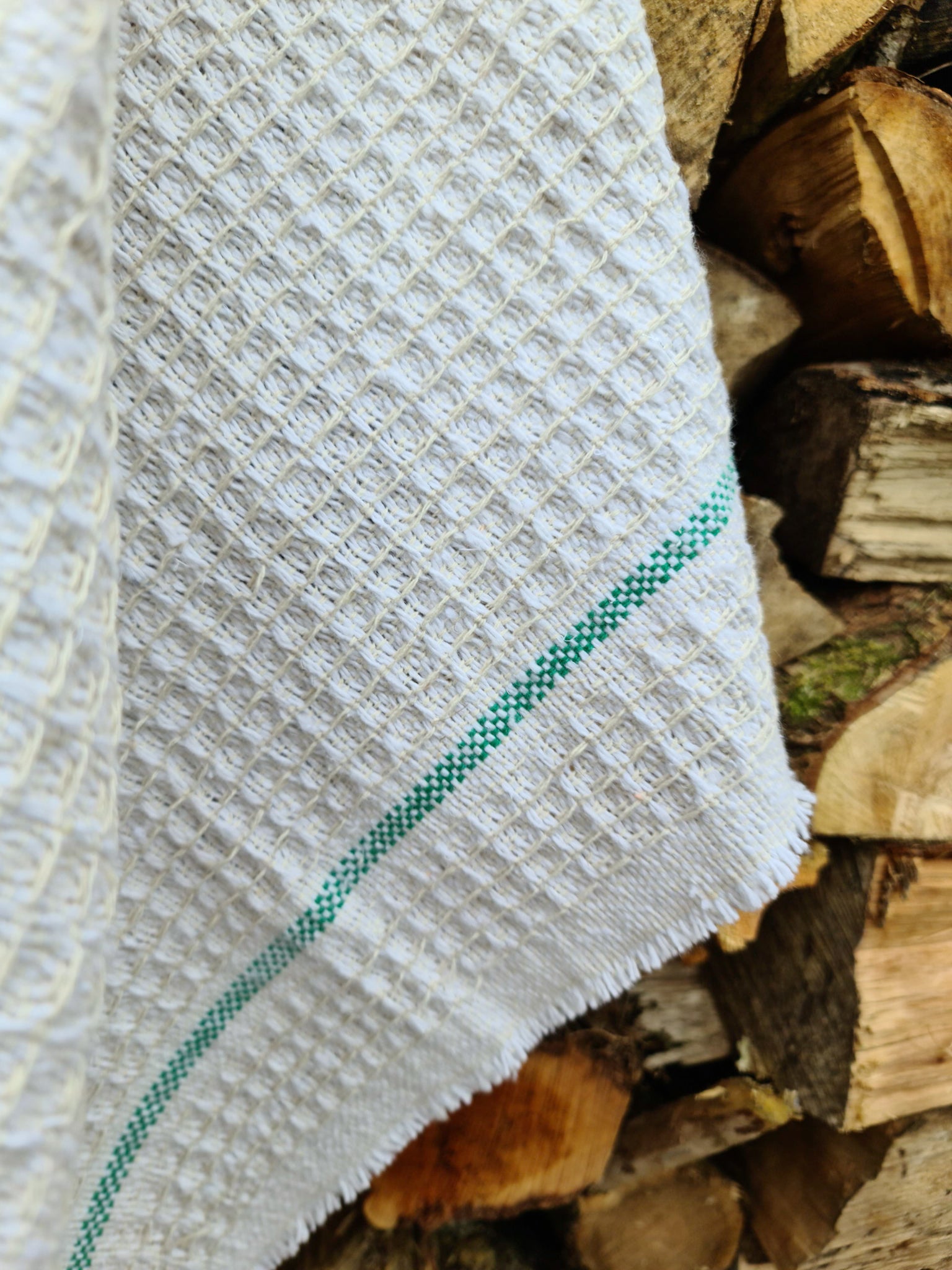 Close up of a white cleaning cloth with green stripes hanging against chopped wood.