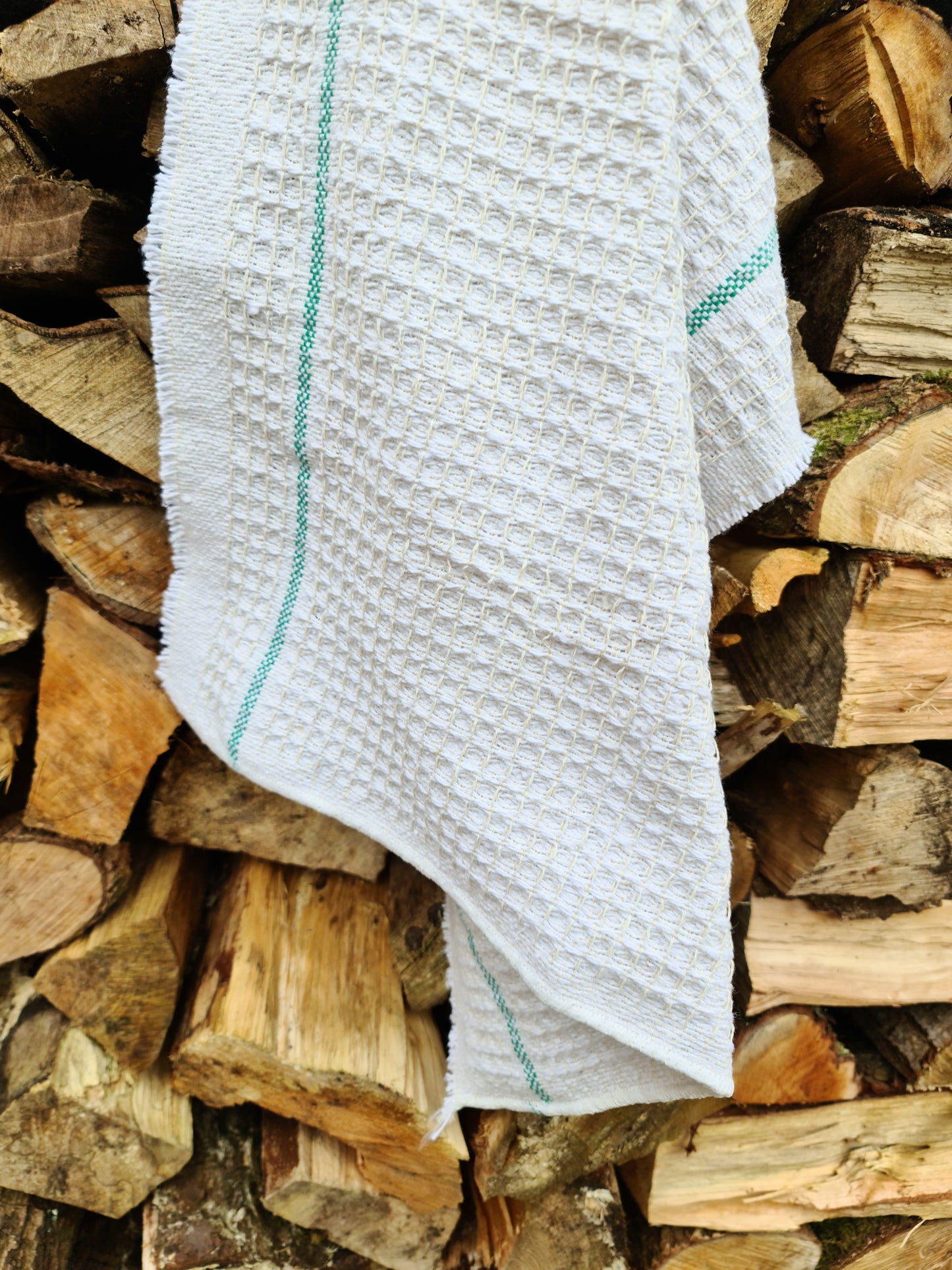 Close up of a white cleaning cloth with green stripes hanging against chopped wood.