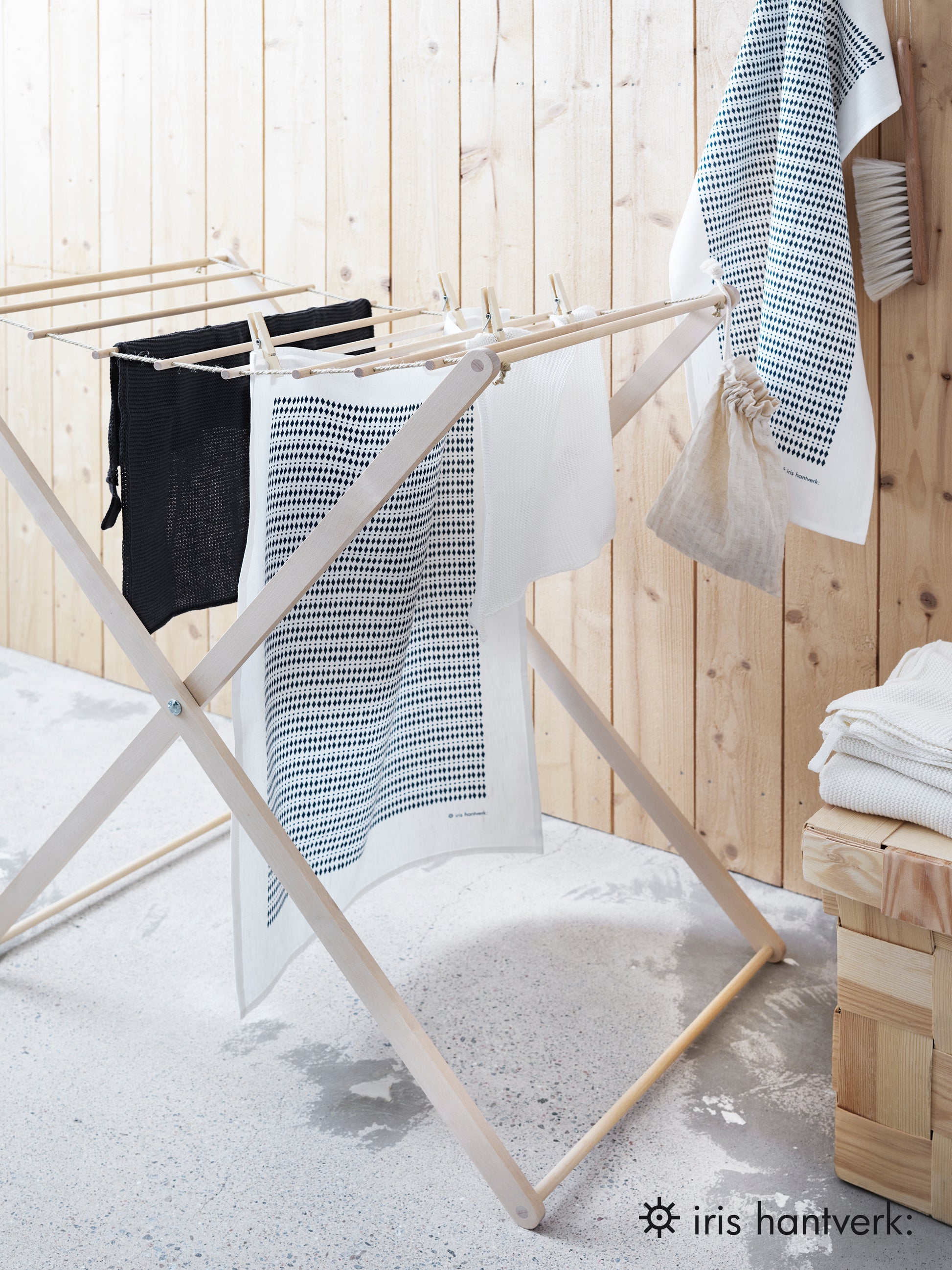 Foldable wooden wash drier airer with clothes drying on it, placed in a wooden room with a wooden wall.