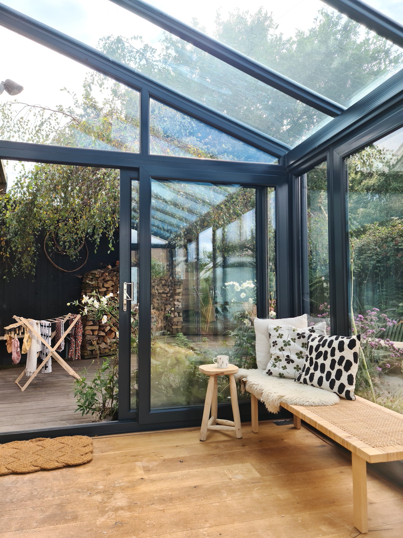 Foldable wooden wash drier airer with clothes drying on it seen from afar in a garden, from the viewpoint of a conservatory style room.