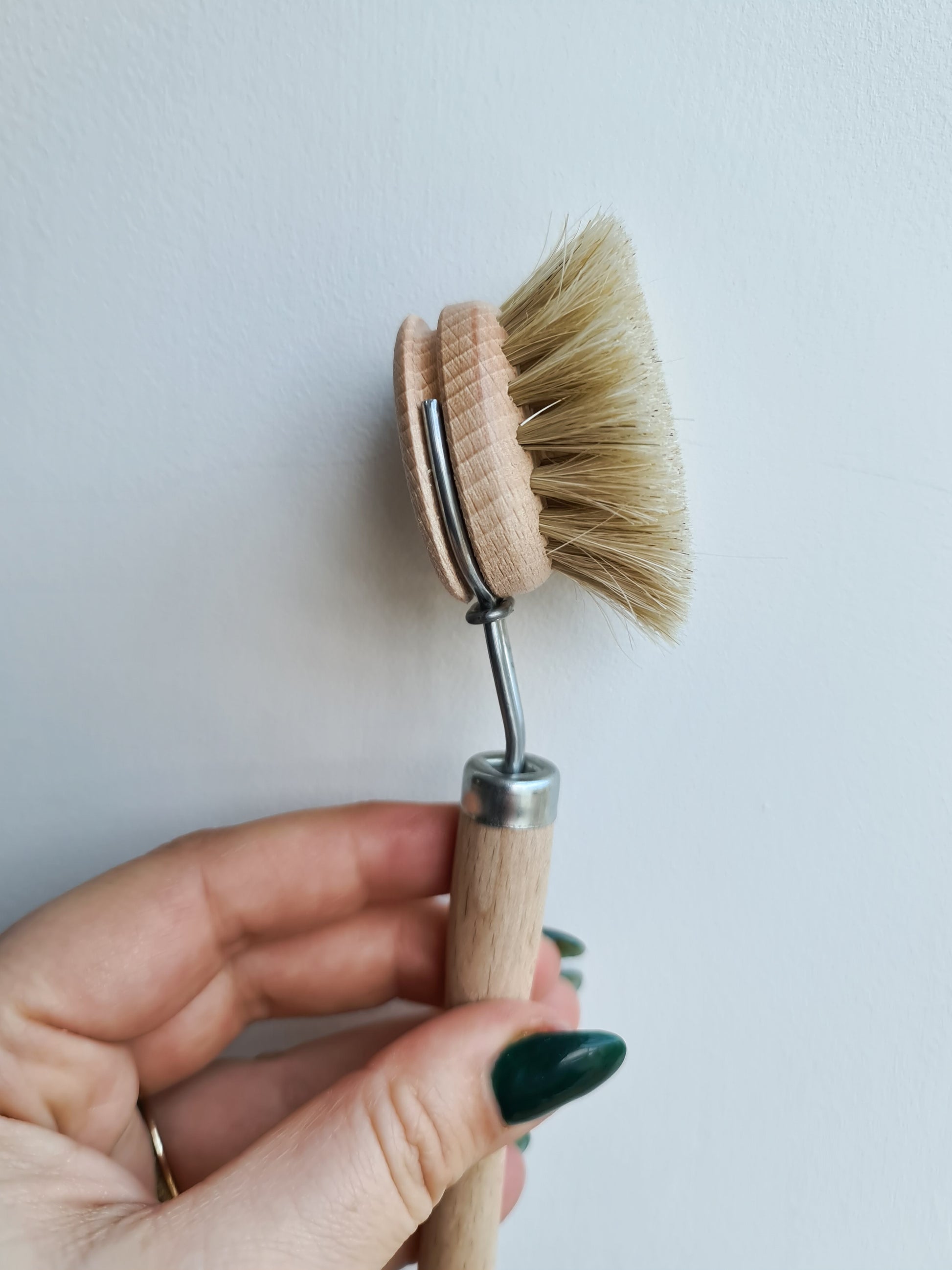 Hand holding up an every day dish brush agaisnt a pale background.