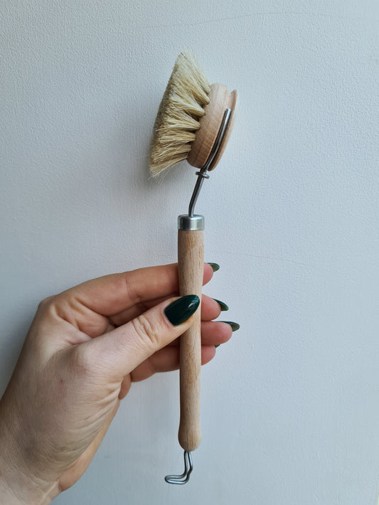 A hand holding a dish brush with a wooden handle and natural bristles.