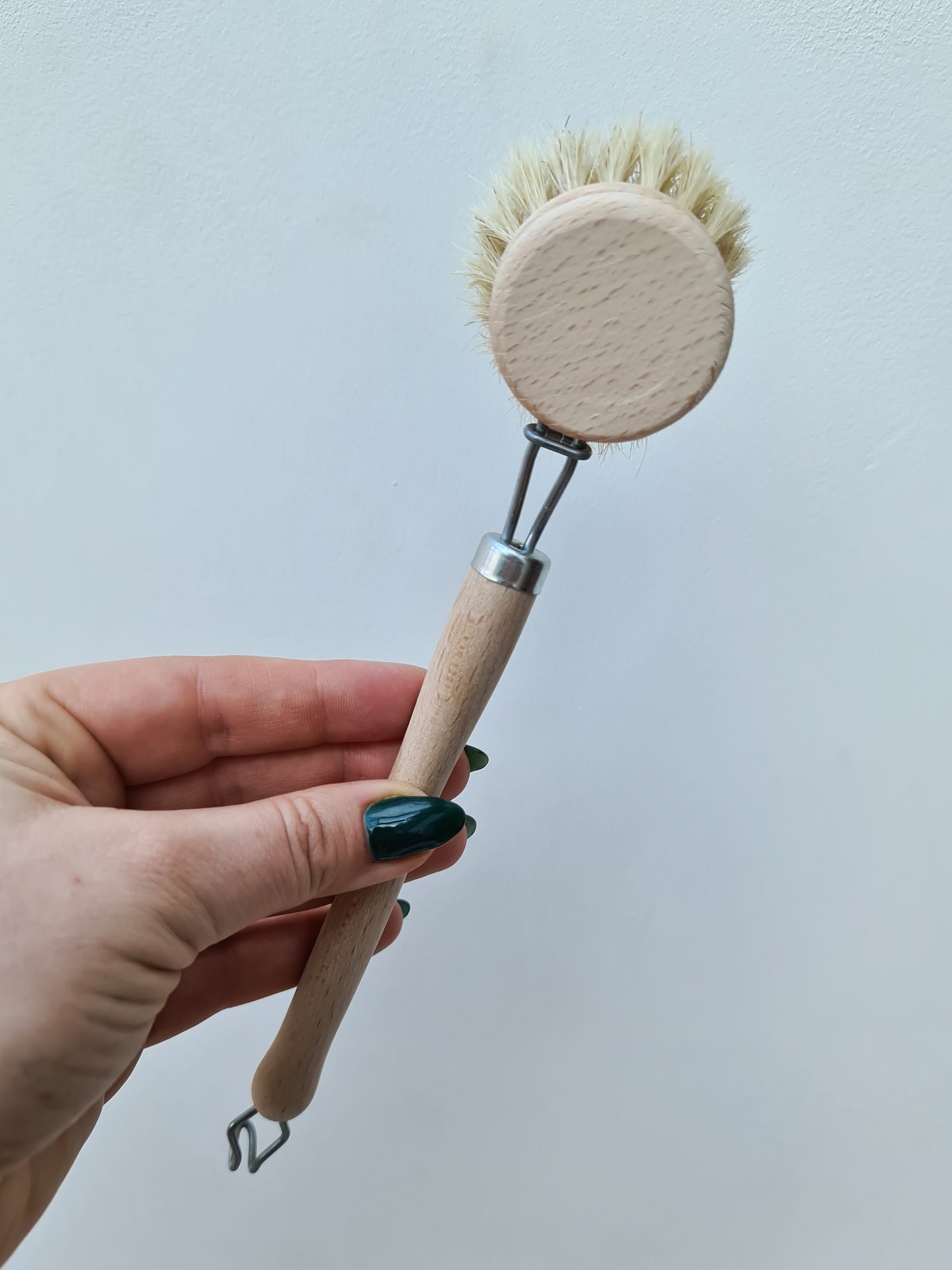 A hand holding a dish brush with a wooden handle and natural bristles.