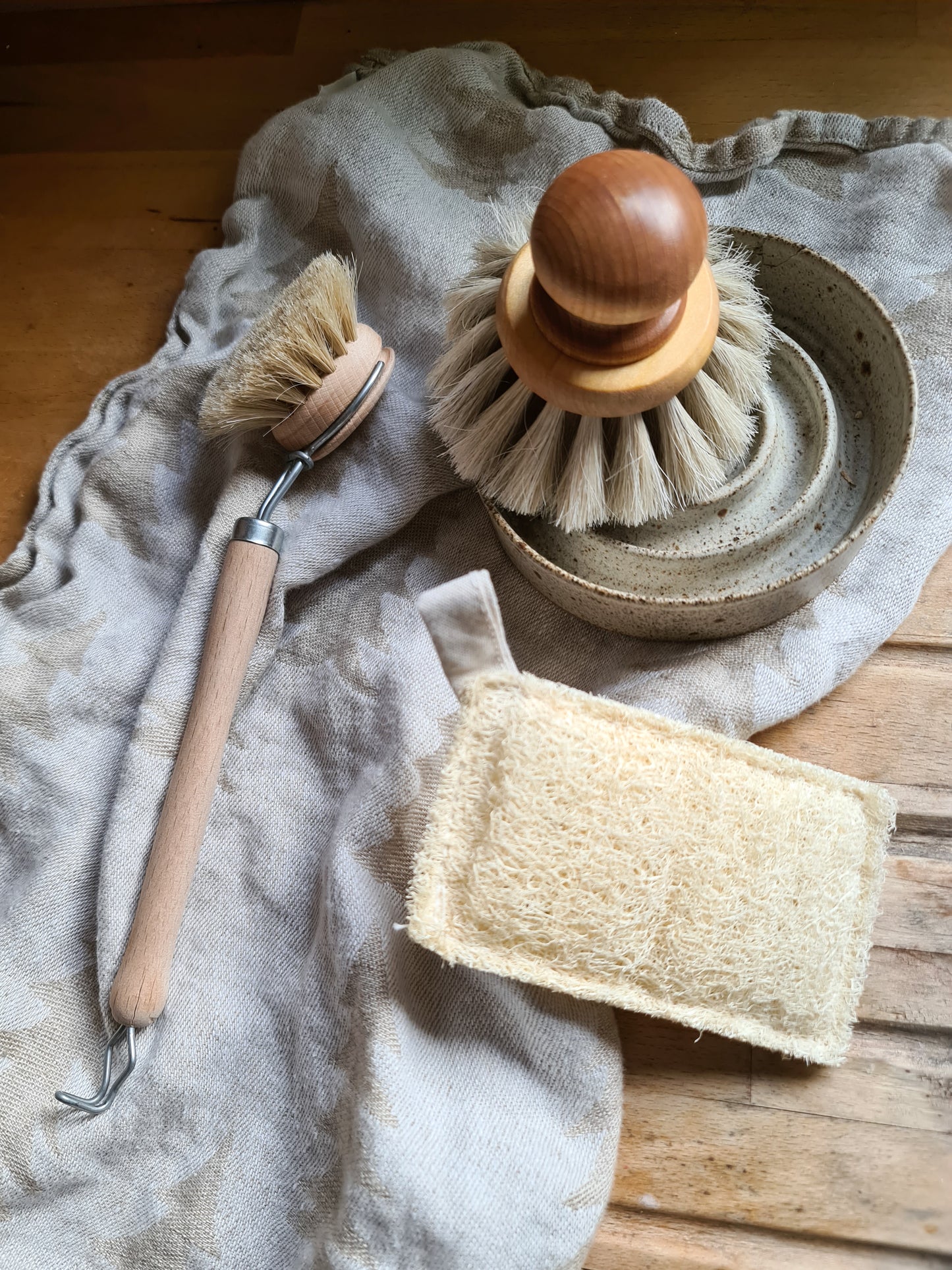 Wooden dish brush resting on a tea towel on a wooden surface, with other kitchen tools next to it. 