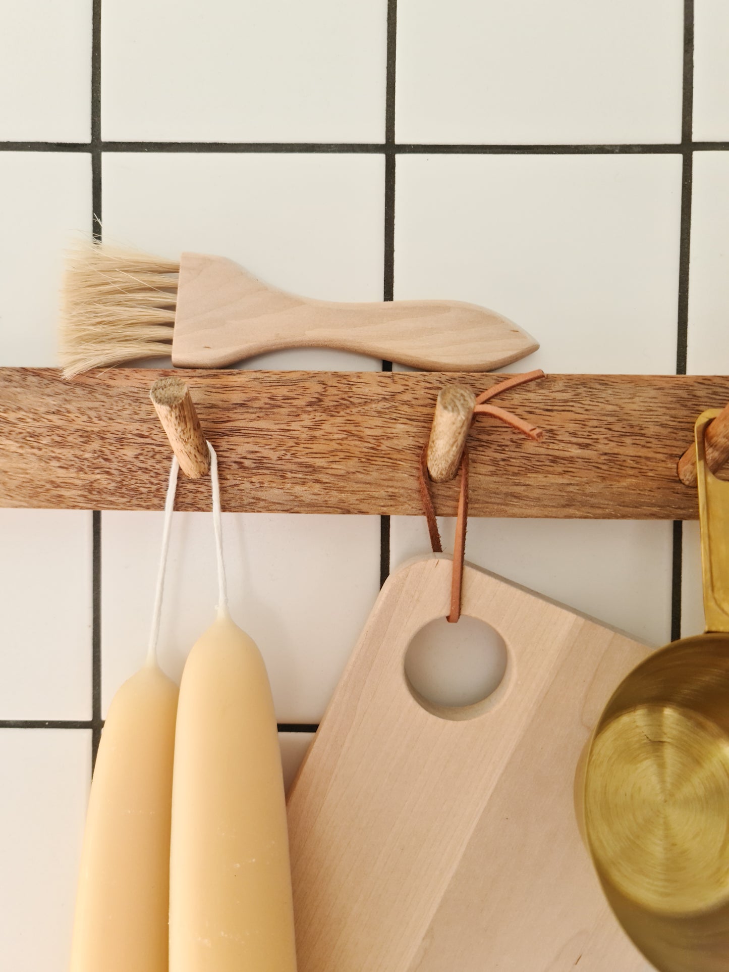 Patry brush made of birch and horsehair sitting atop a peg rail, with various other objects hanging underneath.