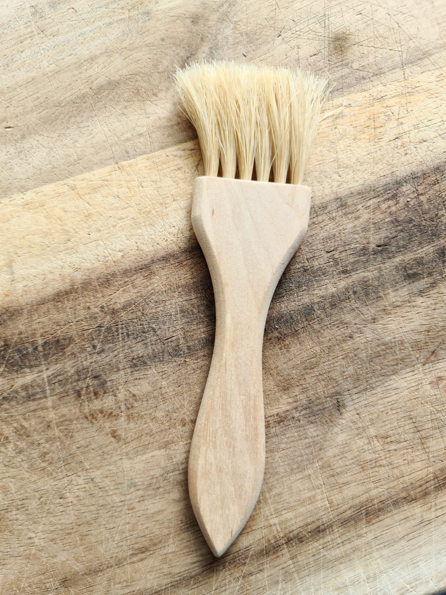 A pastry brush made of birch and horsehair laying against a wooden surface.