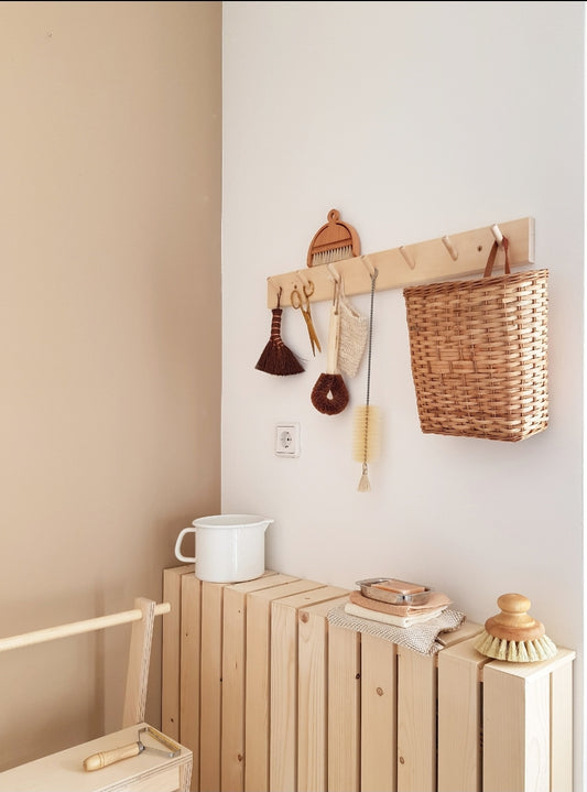 A peg rail rack made of birch wood with multiple hooks, mounted on a wall and holding various items such as towels and a basket.