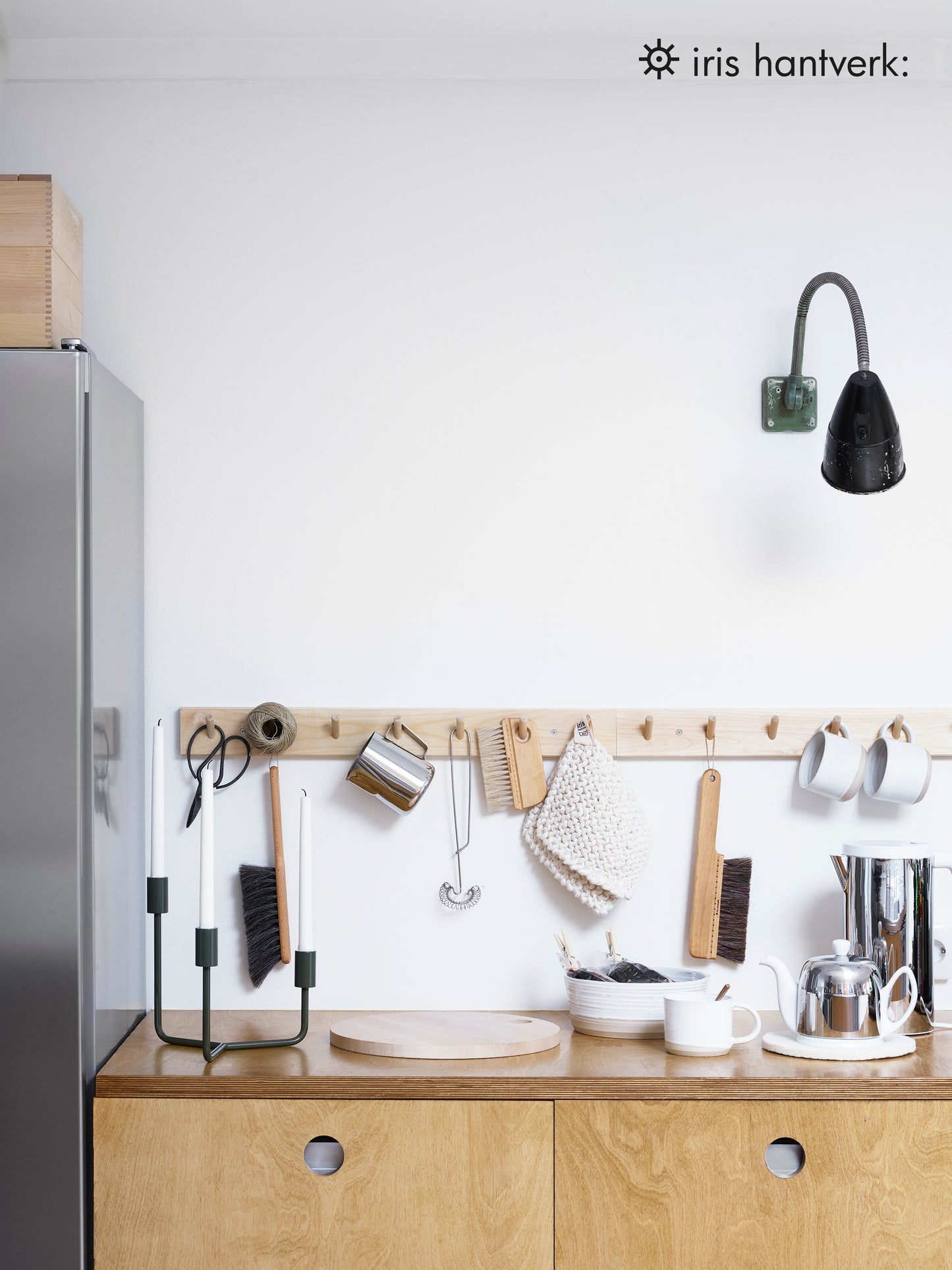 A peg rail rack made of birch wood with multiple hooks, mounted on a wall and holding various kitchen items.