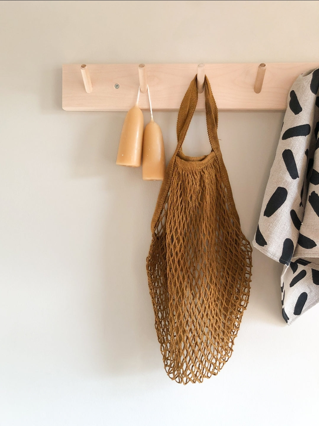 A peg rail rack made of birch wood with multiple hooks, mounted on a wall and holding various items such as towels and a bag.