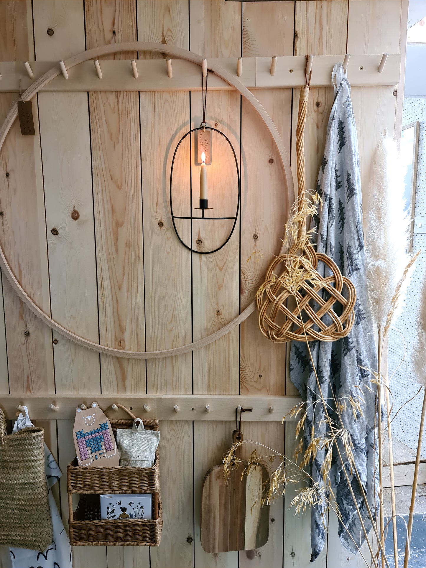 A peg rail rack made of birch wood with multiple hooks, mounted on a wooden clad wall and holding various items such as a towel, wooden hoop, candle holder and rug beater.
