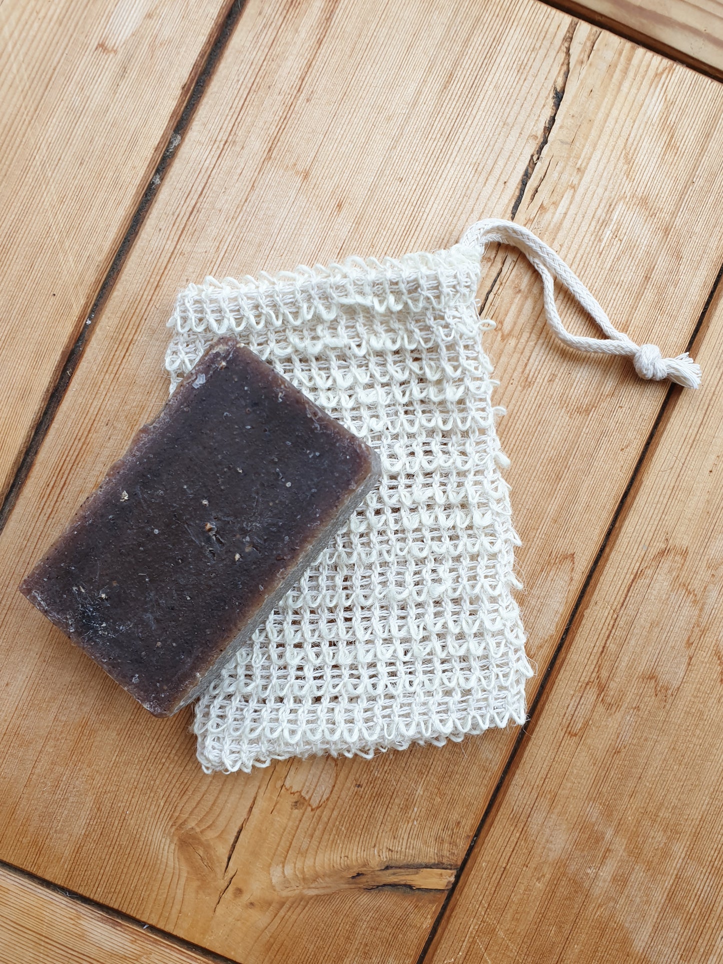 A bar of soap resting on a beige sisal eco soap saver bag with a drawstring, placed on a wooden surface.