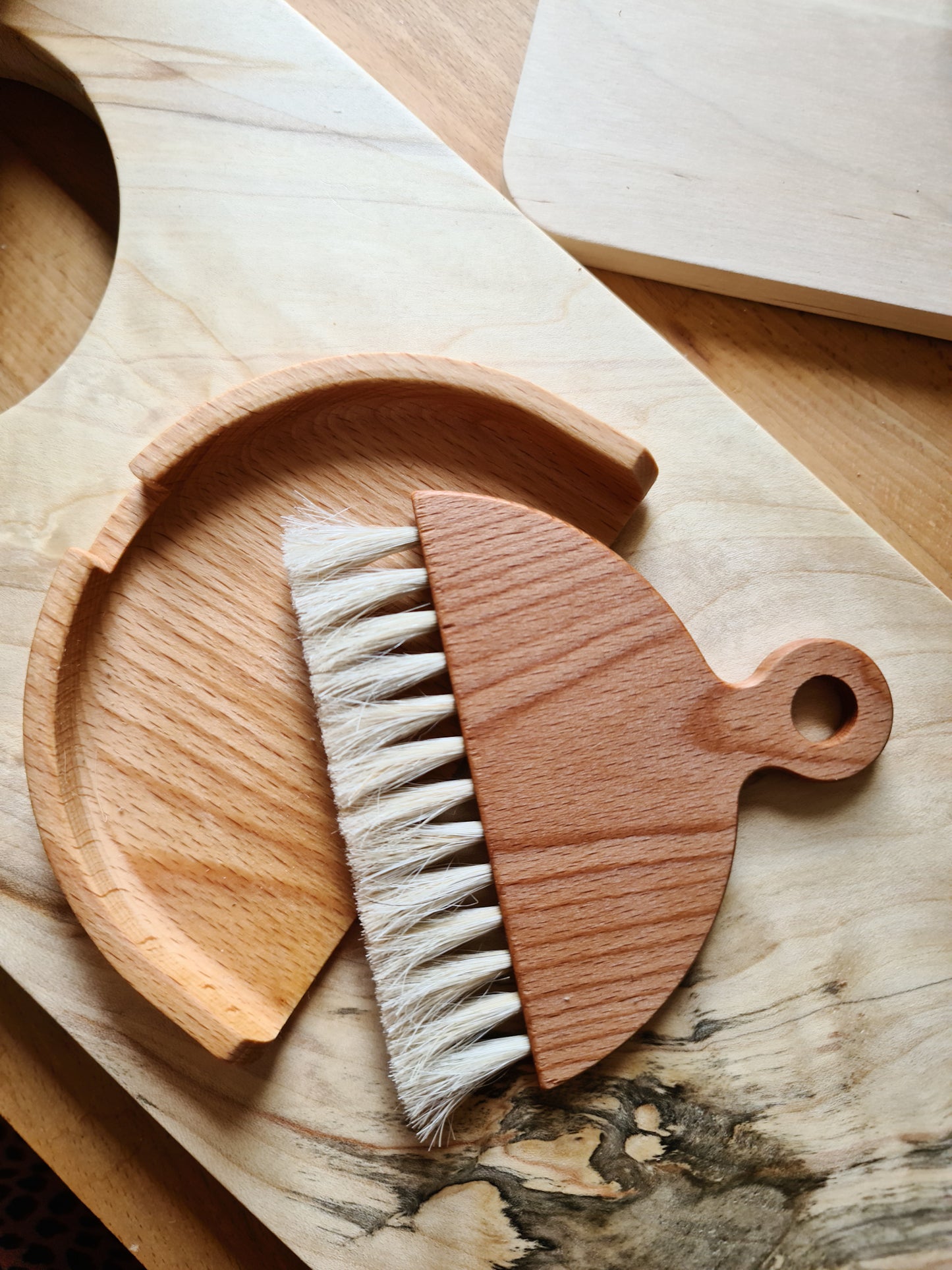 A wooden table brush with a matching dustpan, placed on a wooden surface.