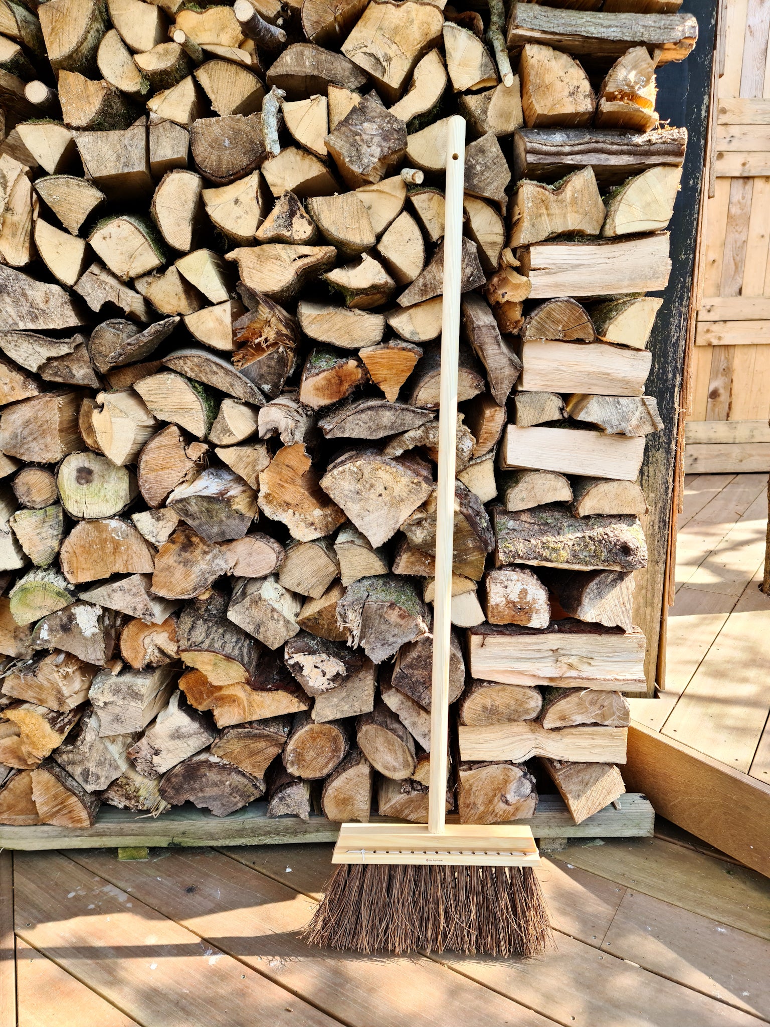 Wooden broom resting against piled wood logs.