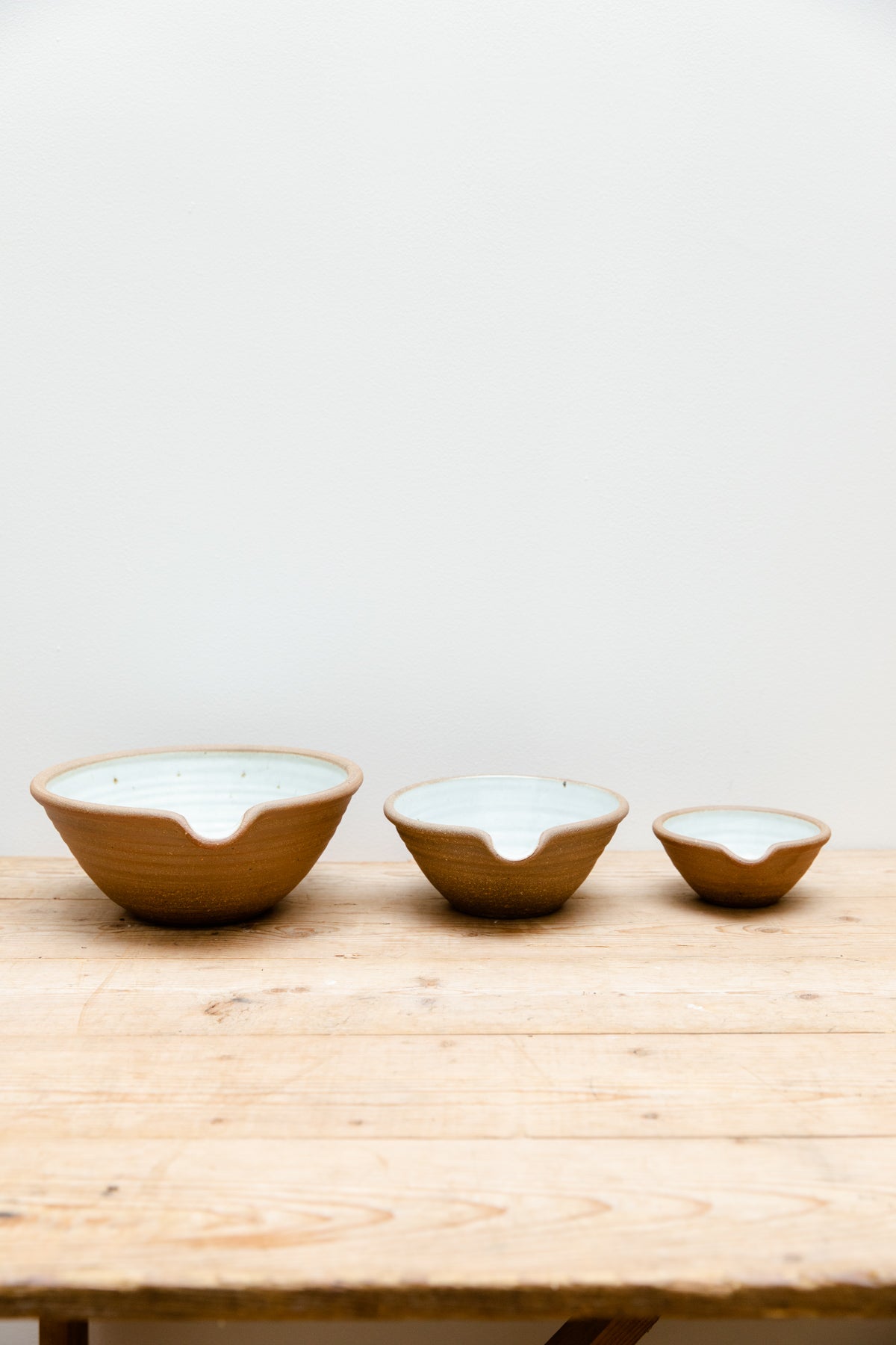 A set of three Leach Pottery mixing bowls in three different sizes displayed on a wooden table.