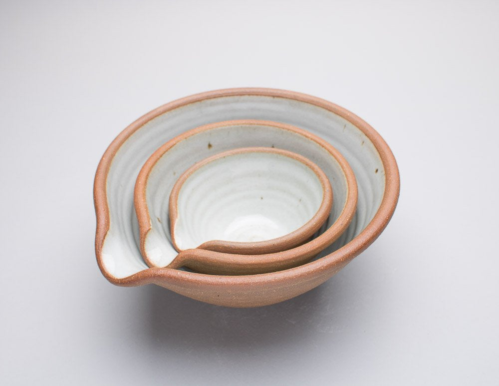 A set of three Leach Pottery mixing bowls nested inside of each other against a white background.