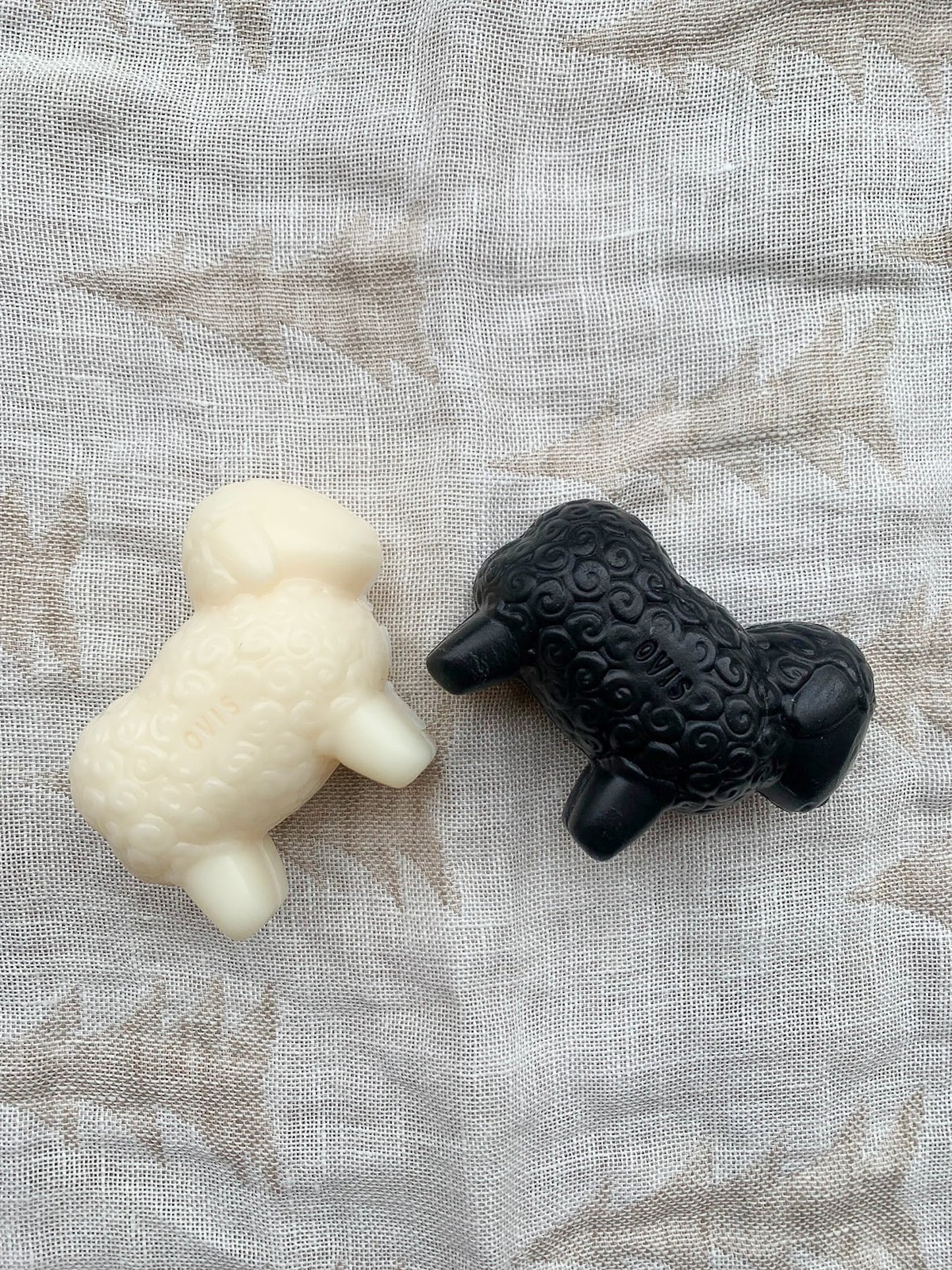 A white sheep-shaped bar of soap and a black version on a textured background.