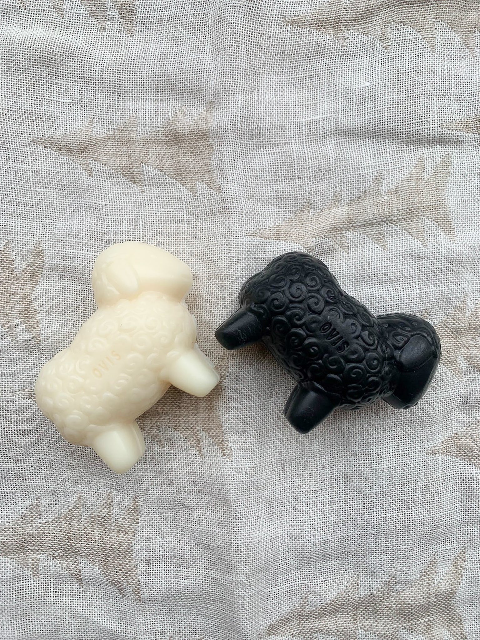 A white sheep-shaped bar of soap and a black version on a textured background.