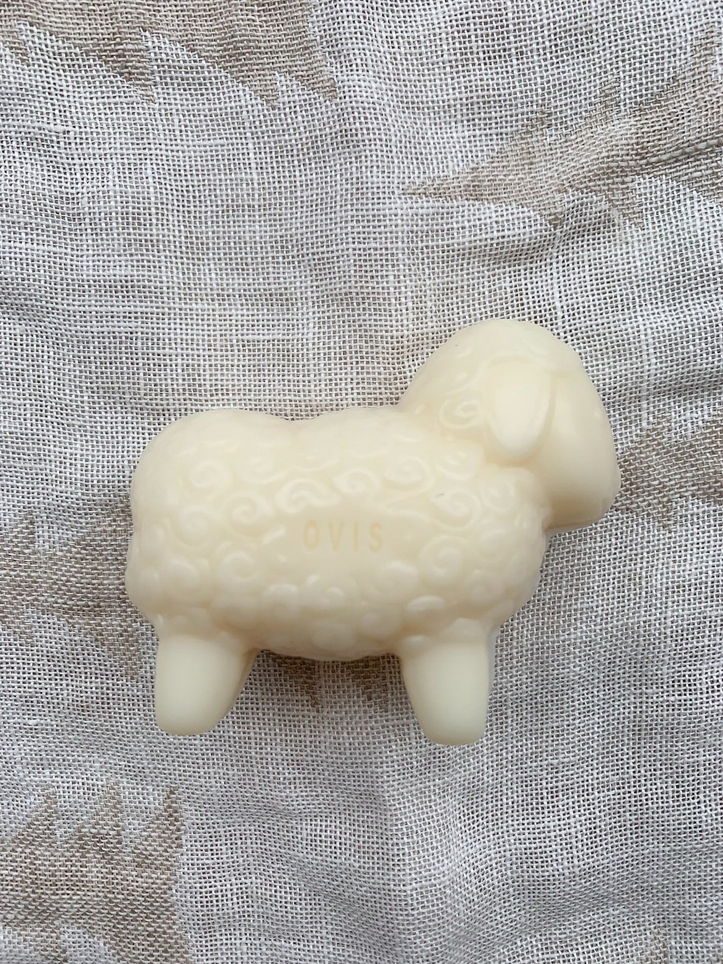 A white, sheep-shaped bar of soap on a textured background.