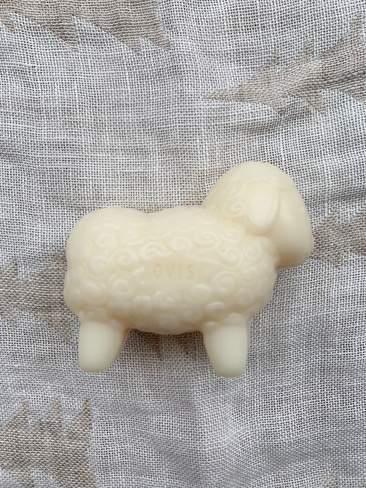 A white, sheep-shaped bar of soap on a textured background.