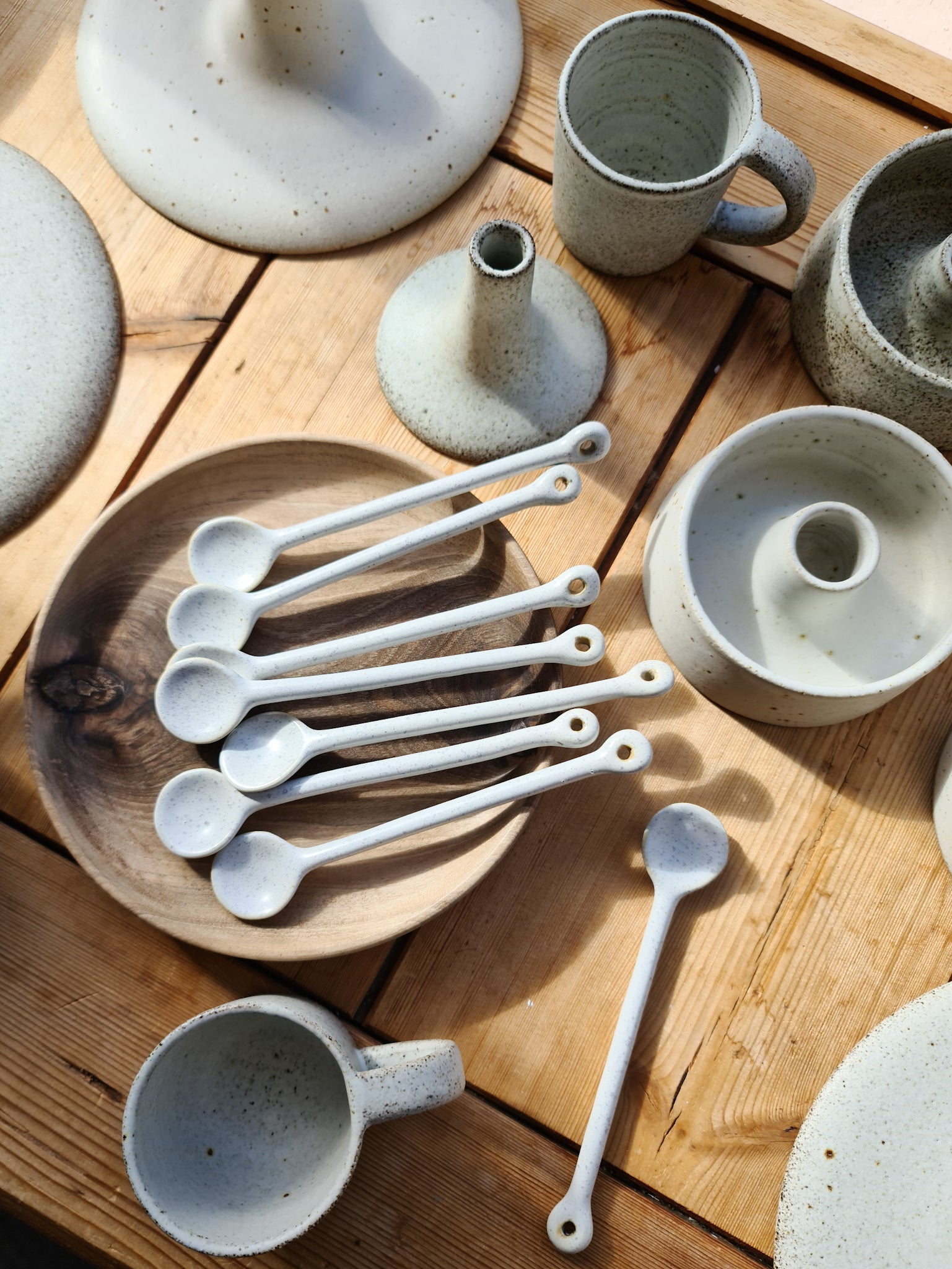 A collection of ceramic tableware including spoons, mugs, and bowls displayed on a wooden table.
