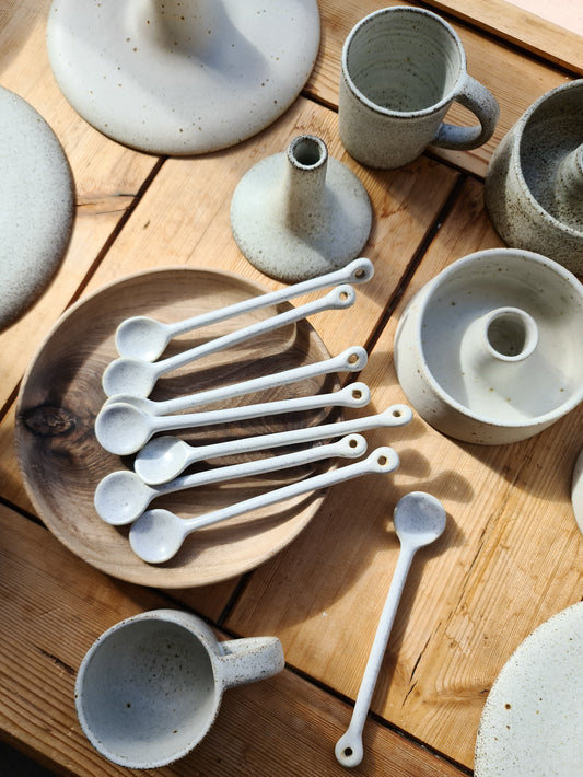 A collection of ceramic tableware including spoons, mugs, and bowls displayed on a wooden table.