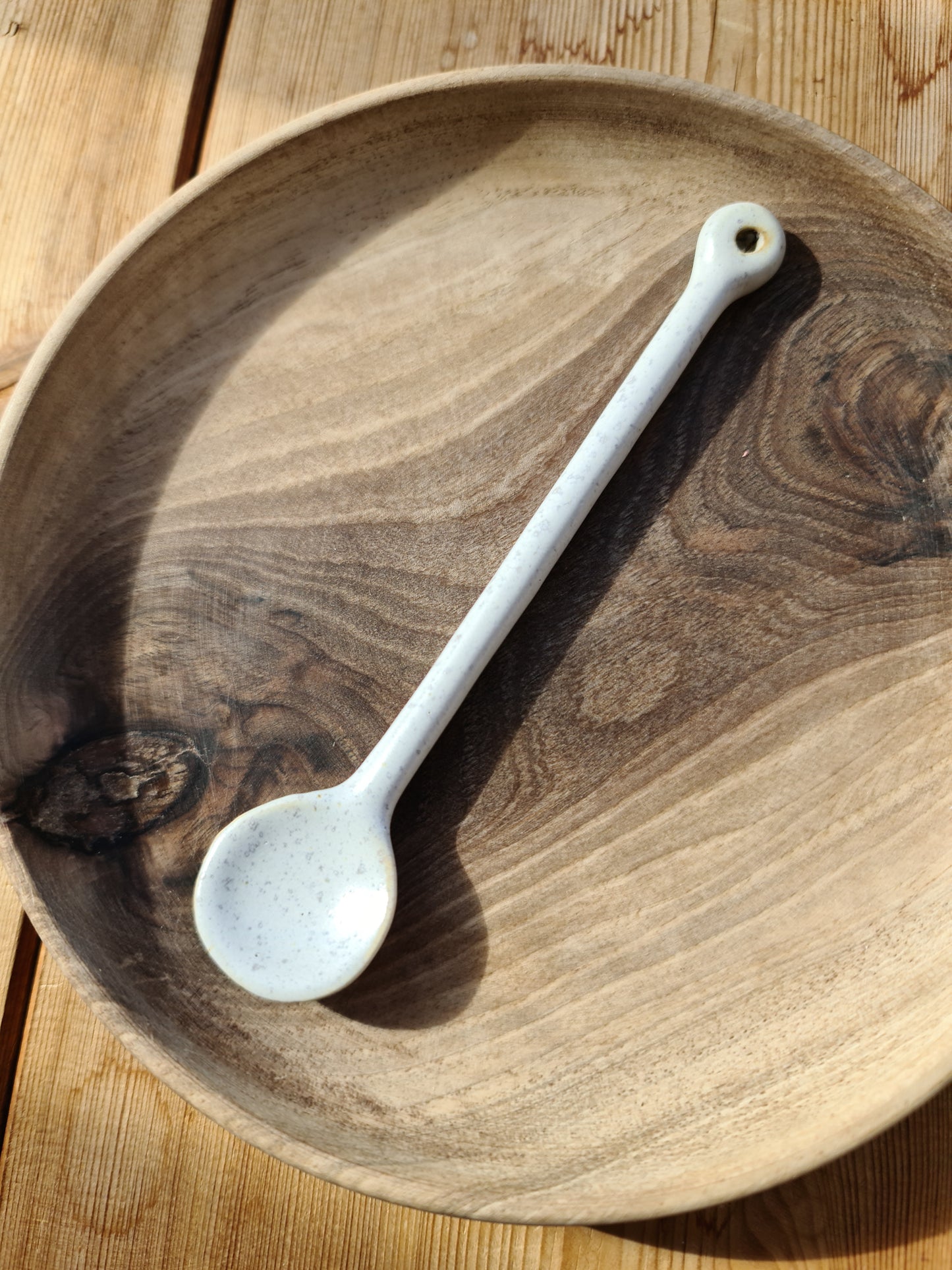 A ceramic white spoon resting on a wooden plate on a wooden table.